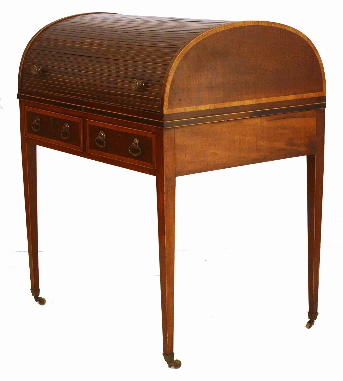 A small George III roll top desk with tambour front. Mahogany with satinwood inlay around drawers and sides. Interior has cubbyholes. Two small drawers and straight legs on casters.