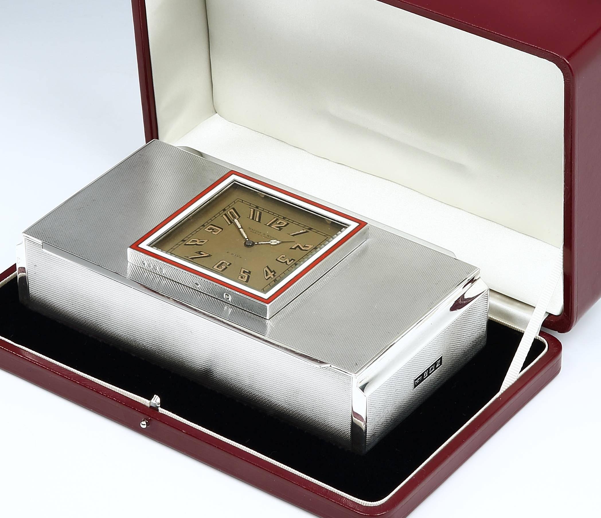 A beautiful quality sterling silver cigarette or cigar box by Mappin & Webb, the geometric-form box with engine-turned panels on each side is surmounted with an 8-day clock, with a gilded face and a red and white enamel surround, marked Mappin &
