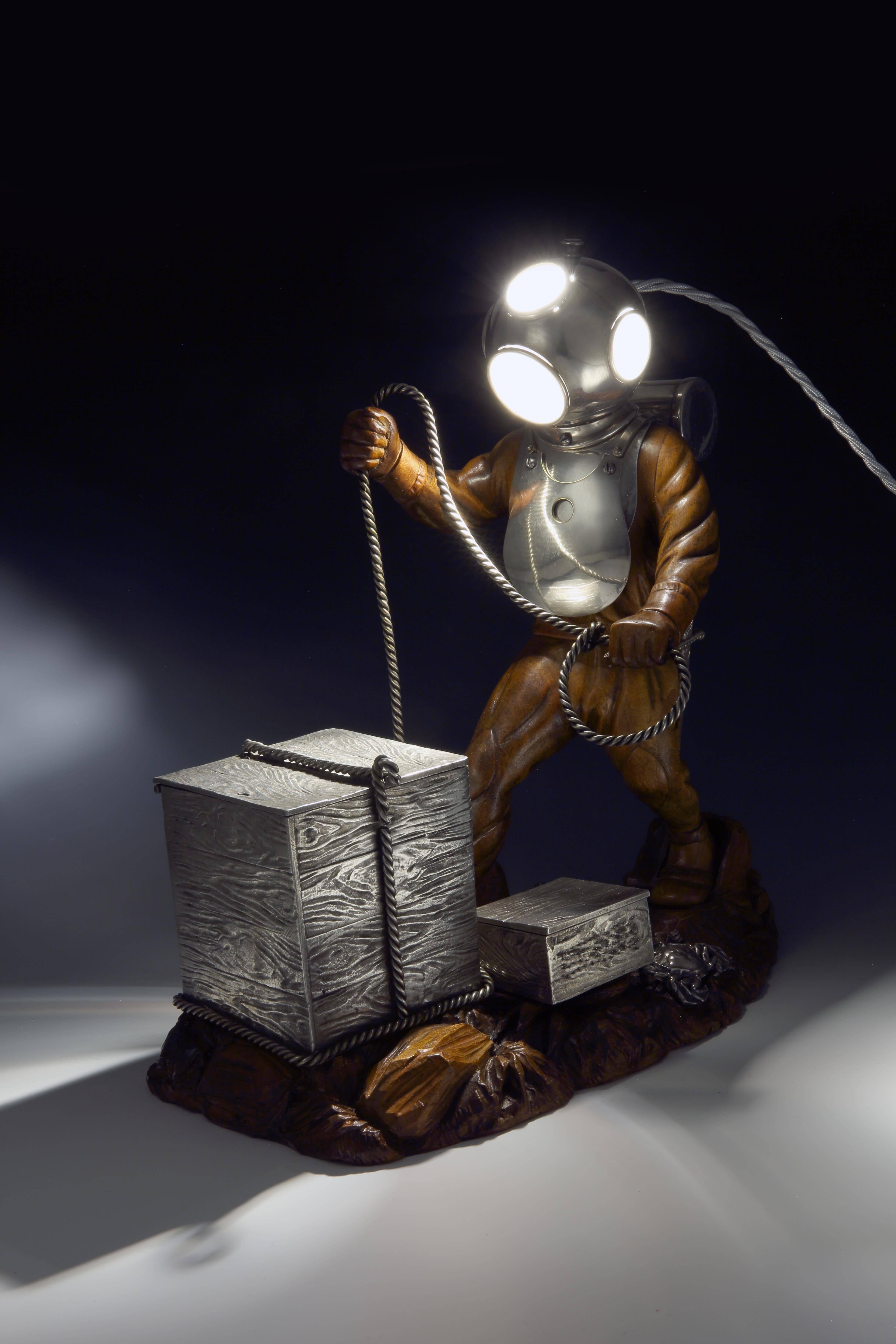 Siebe Gorman, London: a highly unusual table lamp and smoking compendium in the form of a period deep sea diver. The figure in hand-carved fruitwood, is beautifully observed with the detailed folds of his dive suit, stands on a similarly carved