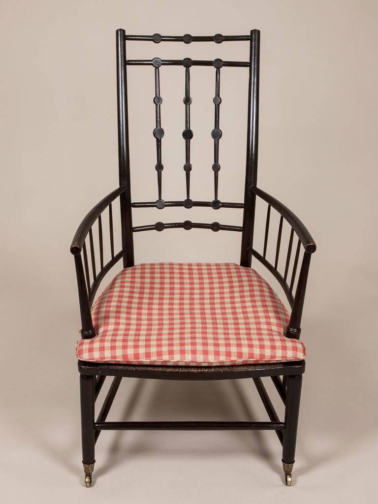 An Arts and Crafts ebonized open armchair with a wide rush seat, circa 1880.