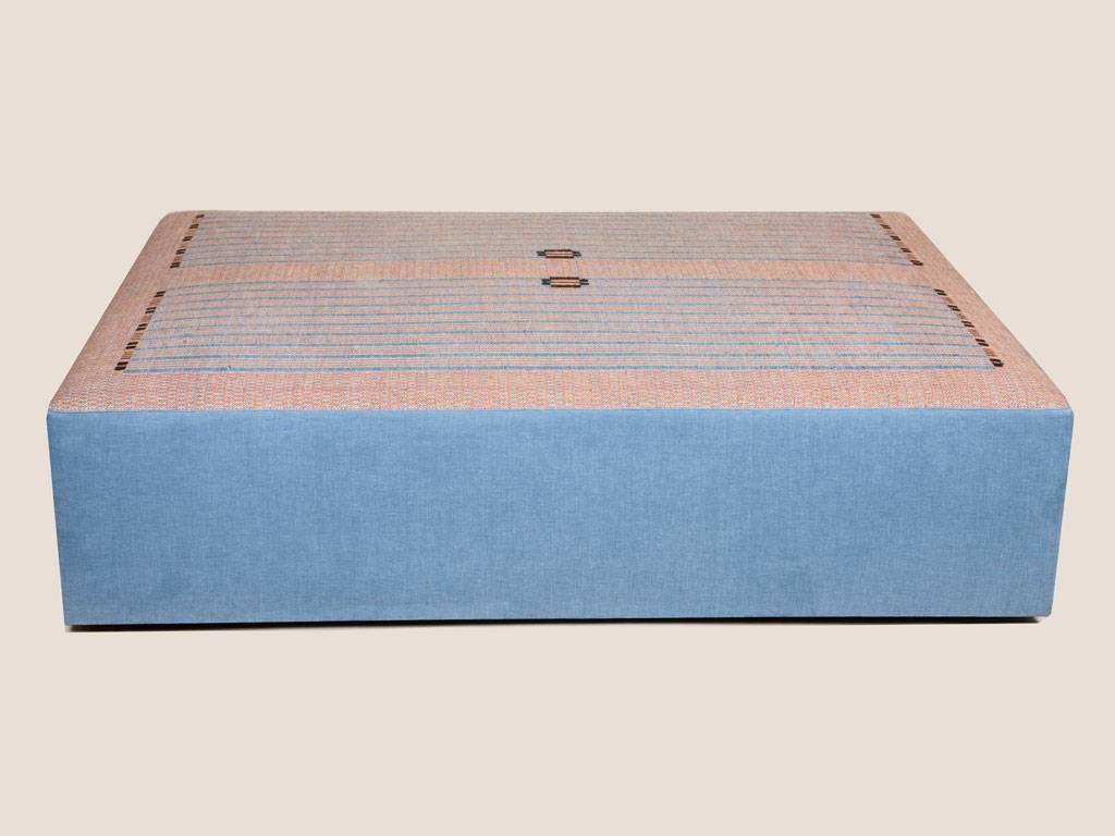 An ottoman with the top a handwoven textile by Kerstin Sundberg-Asling,
in a linear design of oranges and blues.