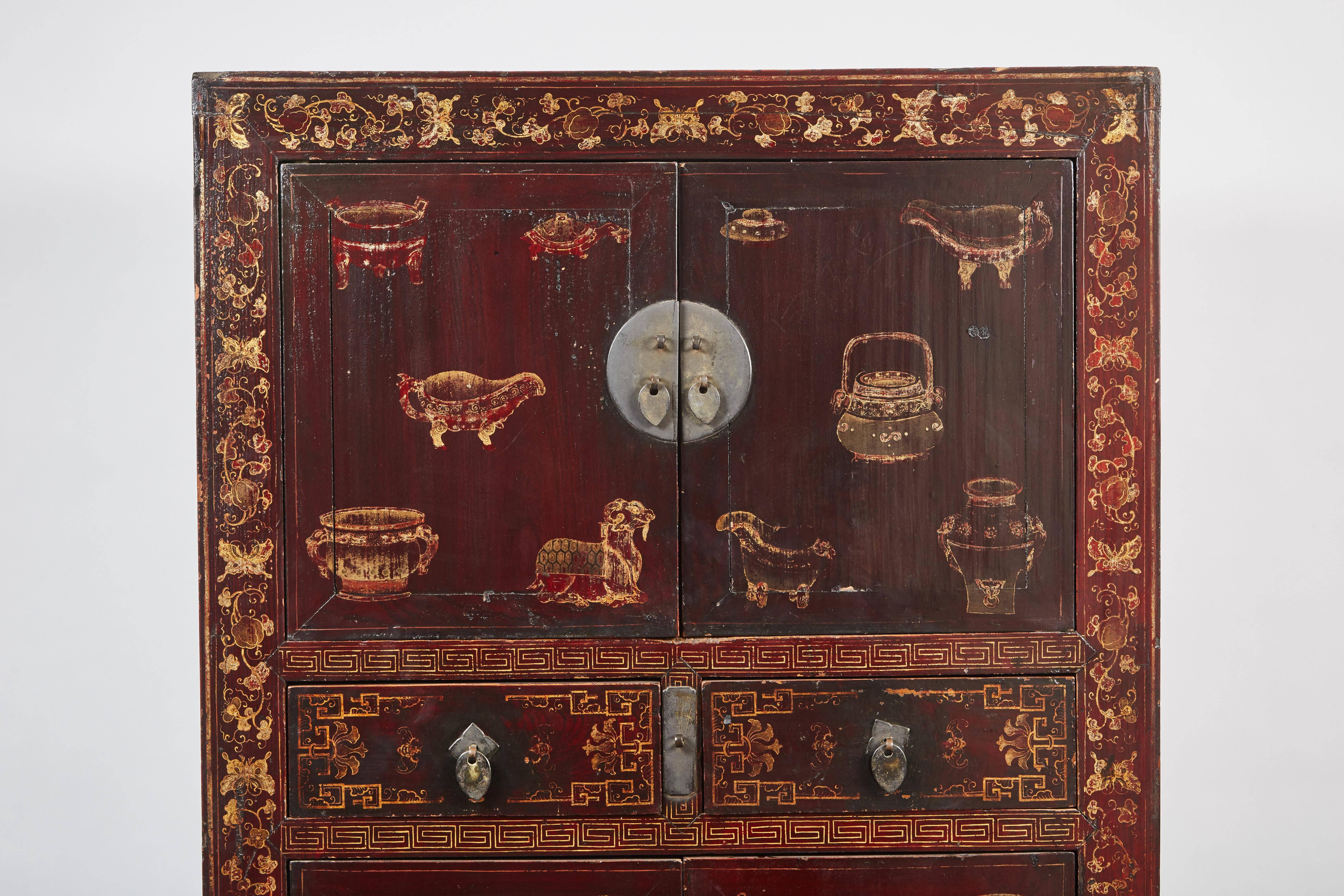 A 18th century oxblood lacquered Chinese cabinet with chinoiserie in the front. The cabinet has two small doors on top, just below are two small drawers and below that are larger doors.