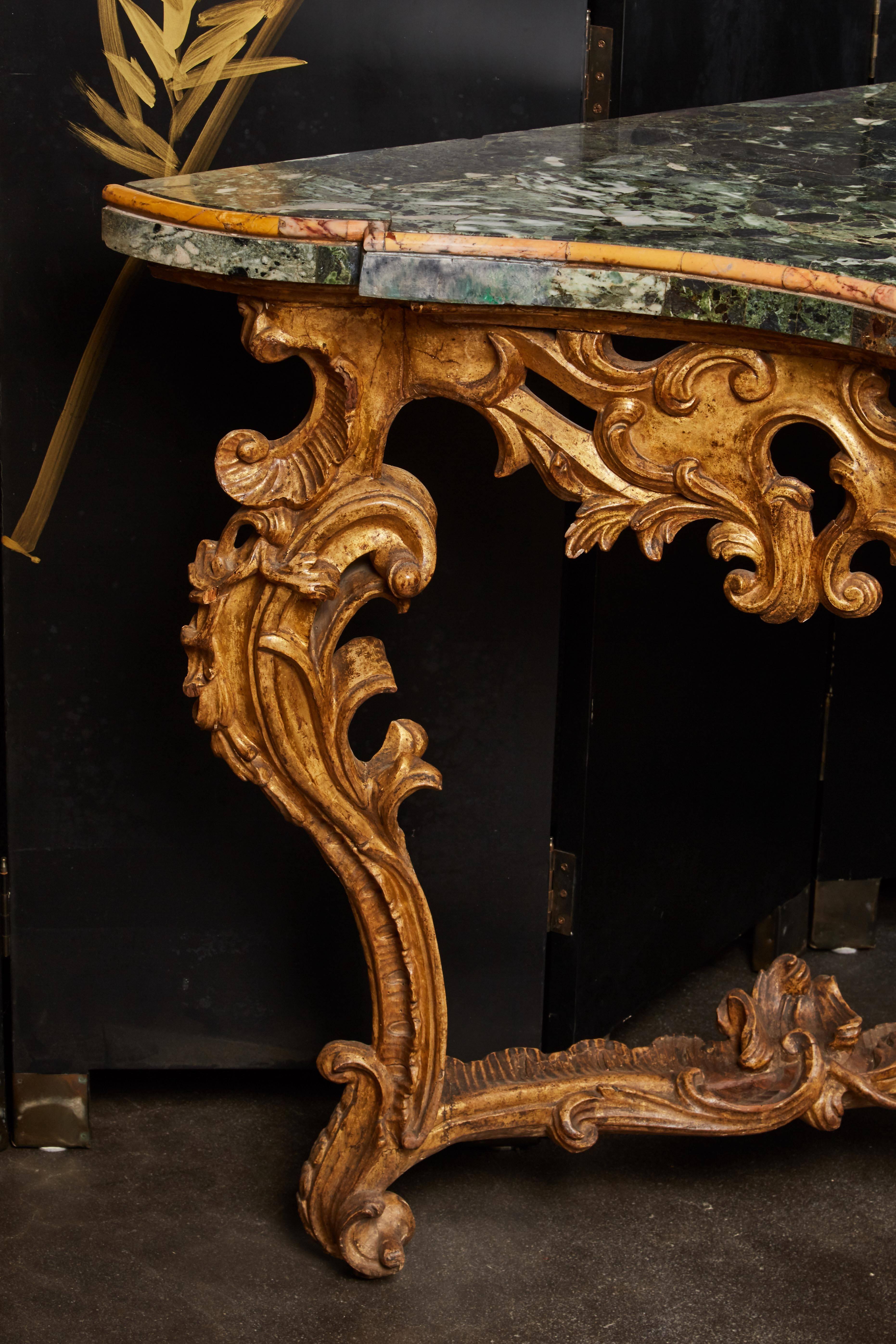 This very large mid-18th century Italian Rococo giltwood green marble top console having a modern marble top; the frame with pierced Giltwood carvings in high Rococo relief, with very large, carved foliage rocaille and scroll work to the apron, the
