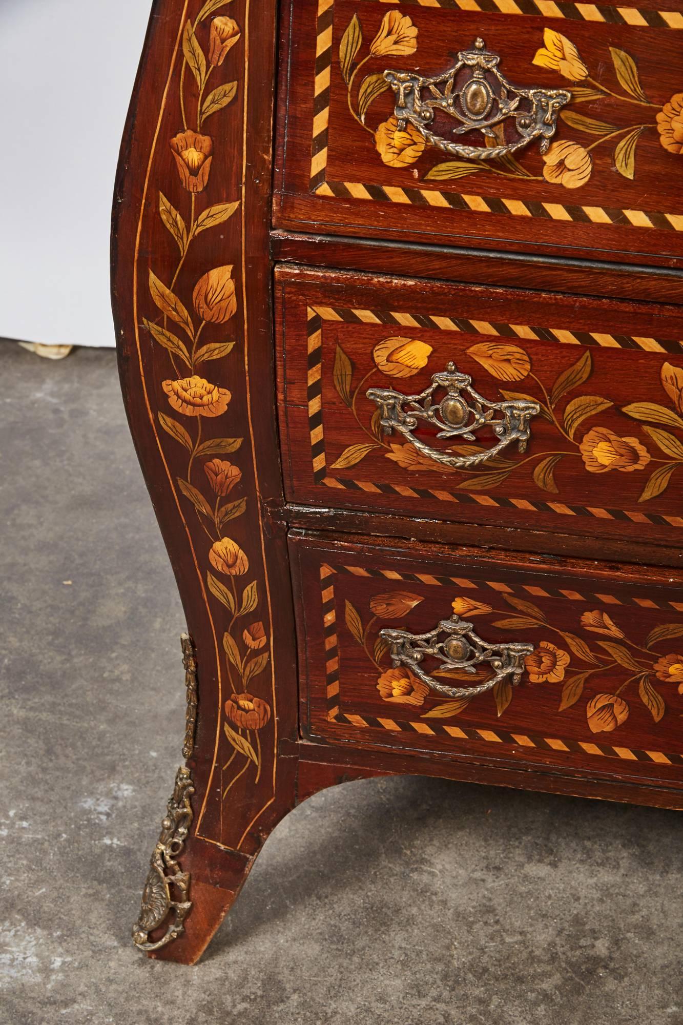 A highly decorated three-drawer Dutch mahogany bow front chest with inlaid foliage, bird and rocaille motifs in yellow toned and green toned woods.
  