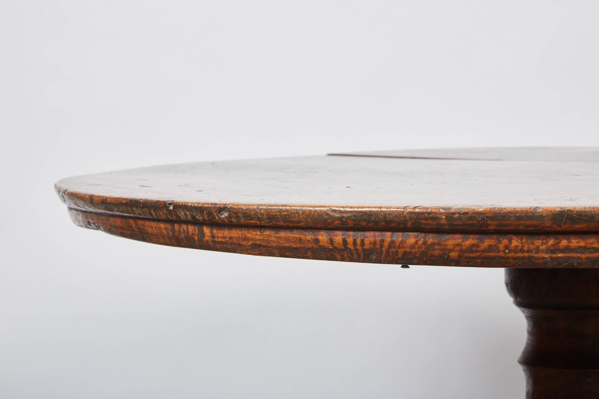 A simple Indonesian teak pedestal table standing on three legs carved out to represent a foliage design.