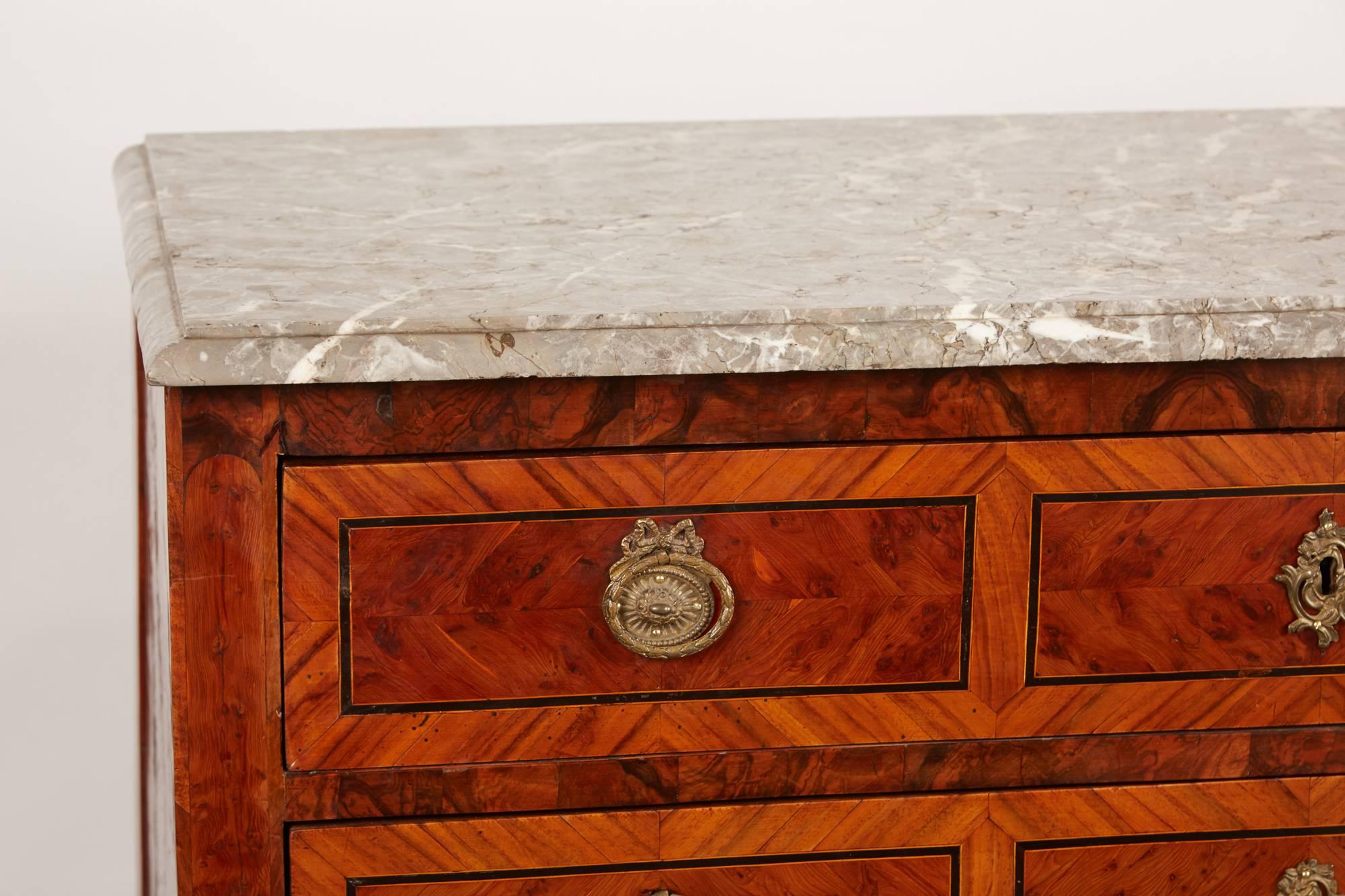 An 18th century Italian neoclassical style marble chest of drawers featuring contrasting marquetry inlay throughout the exterior as well as decorative rose colored paper lines throughout the drawer faces. The chest of drawers has a marble top with