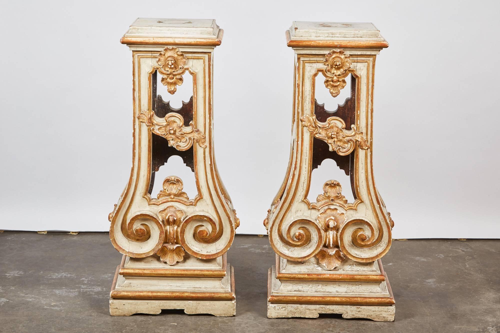 Each of these Italian, 18th century Rococo cream painted and parcel-gilt pedestal stand has a square top over a molded and gilt rim over a rectangular open section with scrolls and rocaille and gilt edges; the lower front section has whorls. Each