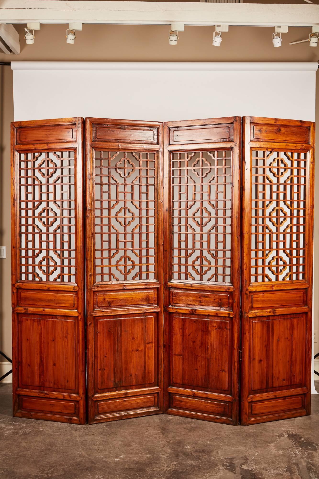A set of 12 brown double-sided late 19th century carved Chinese screens that feature an upper portion of intricate geometrical patterns and a lower portion consisting of solid wood panels.