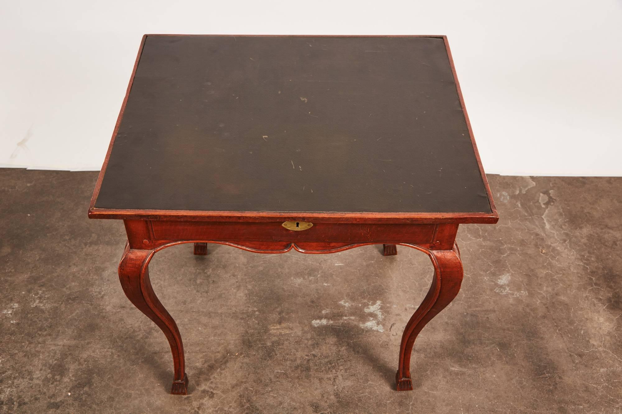 A late 18th century French beech Louis XV game table consisting of faded red paint overall and a black leather top later applied. Its characteristics are a set of four simplistic cabriole legs, four high center pivots and exposed nailheads.