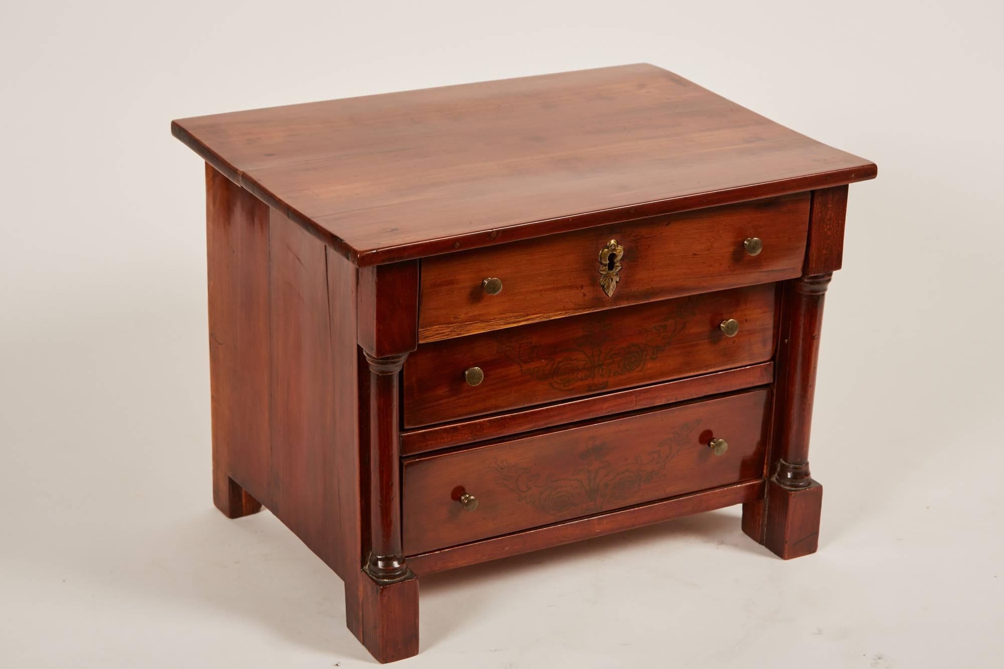 A remarkable late 19th century mini sample chest of drawers made of mahogany wood and of the Empire style, featuring design characteristics such as a pair of columns and etches of foliage designs which creates a classic example of Empire design.