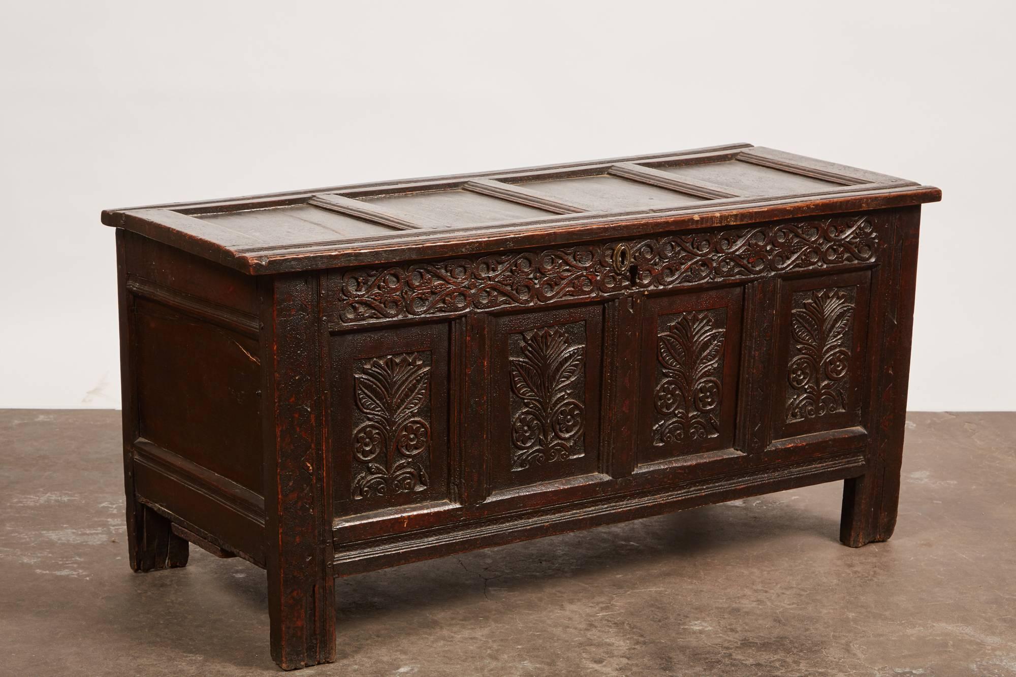 This late 18th century English carved oak trunk features intricate carvings on the facade. There are four panels with identical abstract flowers on each, as well as a row of continuous foliage designs carved above the panels.