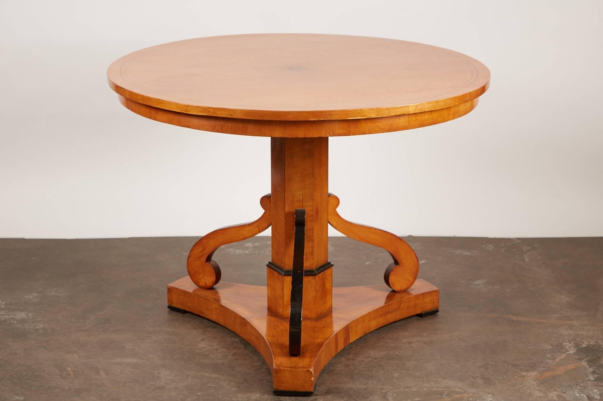 An early 20th century Swedish ebonized cheerywood second period Biedermeier pedestal table featuring a set of three scroll cut supports that surround a center octagonal pillar atop a triangle base.