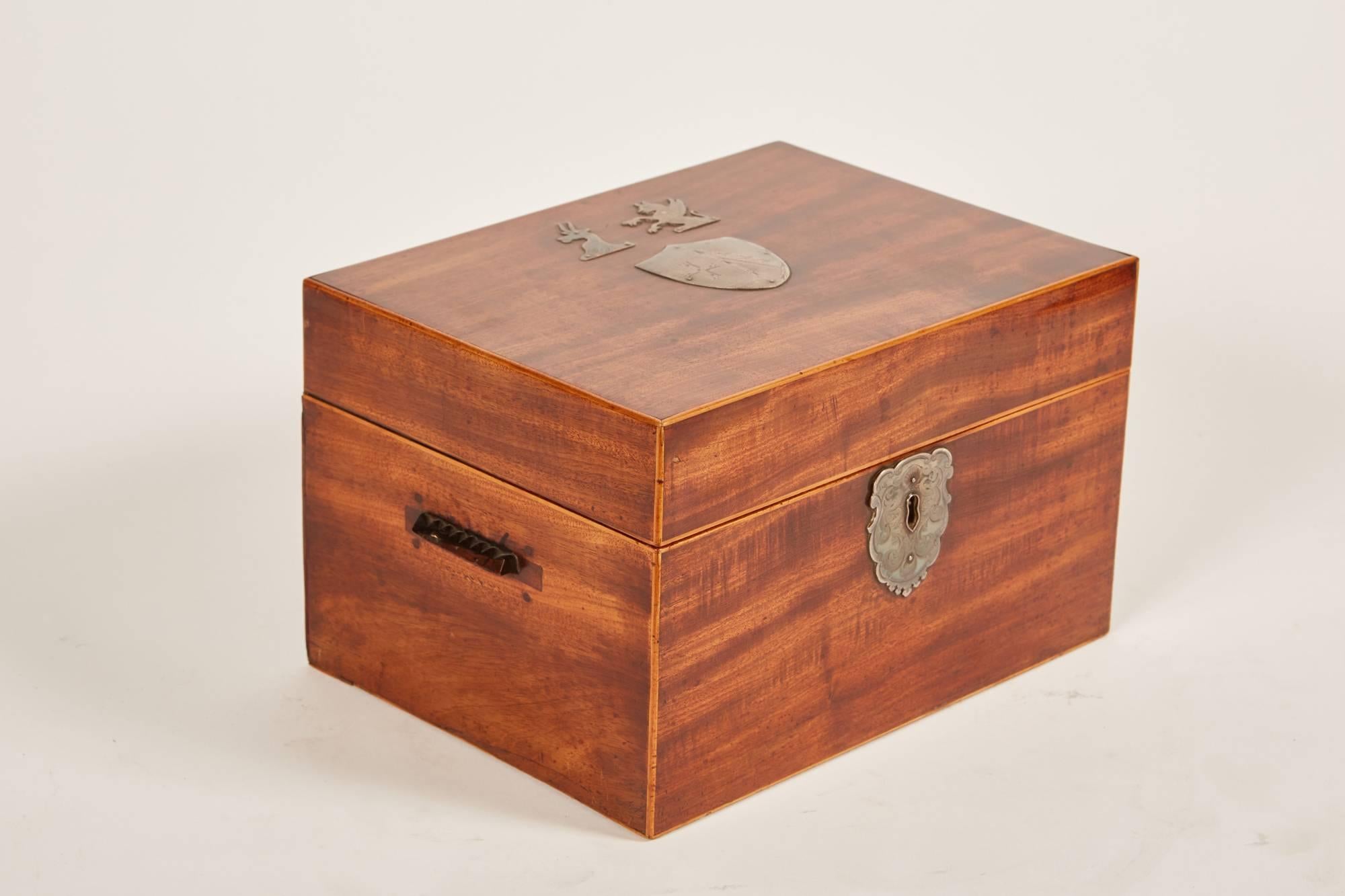 A 19th century mahogany English Regency tea caddy with silver markings of a family crest, griffon and ram on the top. The interior of this tea caddy encloses a pair of metal lined storage compartments.