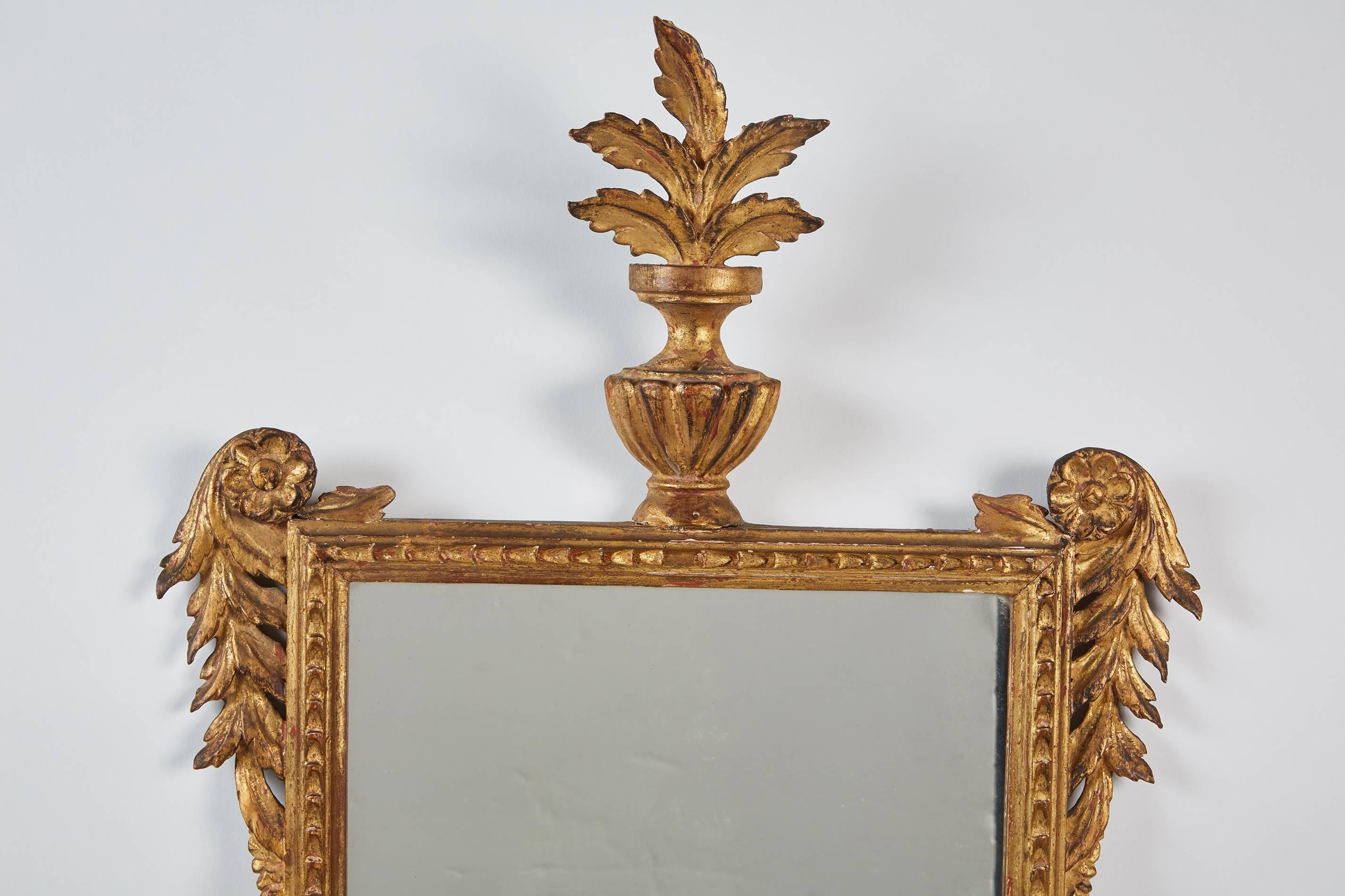 An 18th century French Regency gilt mirror featuring beautifully carved flowers and acanthus leaves draping along the side of the rectilinear frame, the mirror also consists of a Classic urn crest sitting at the top.