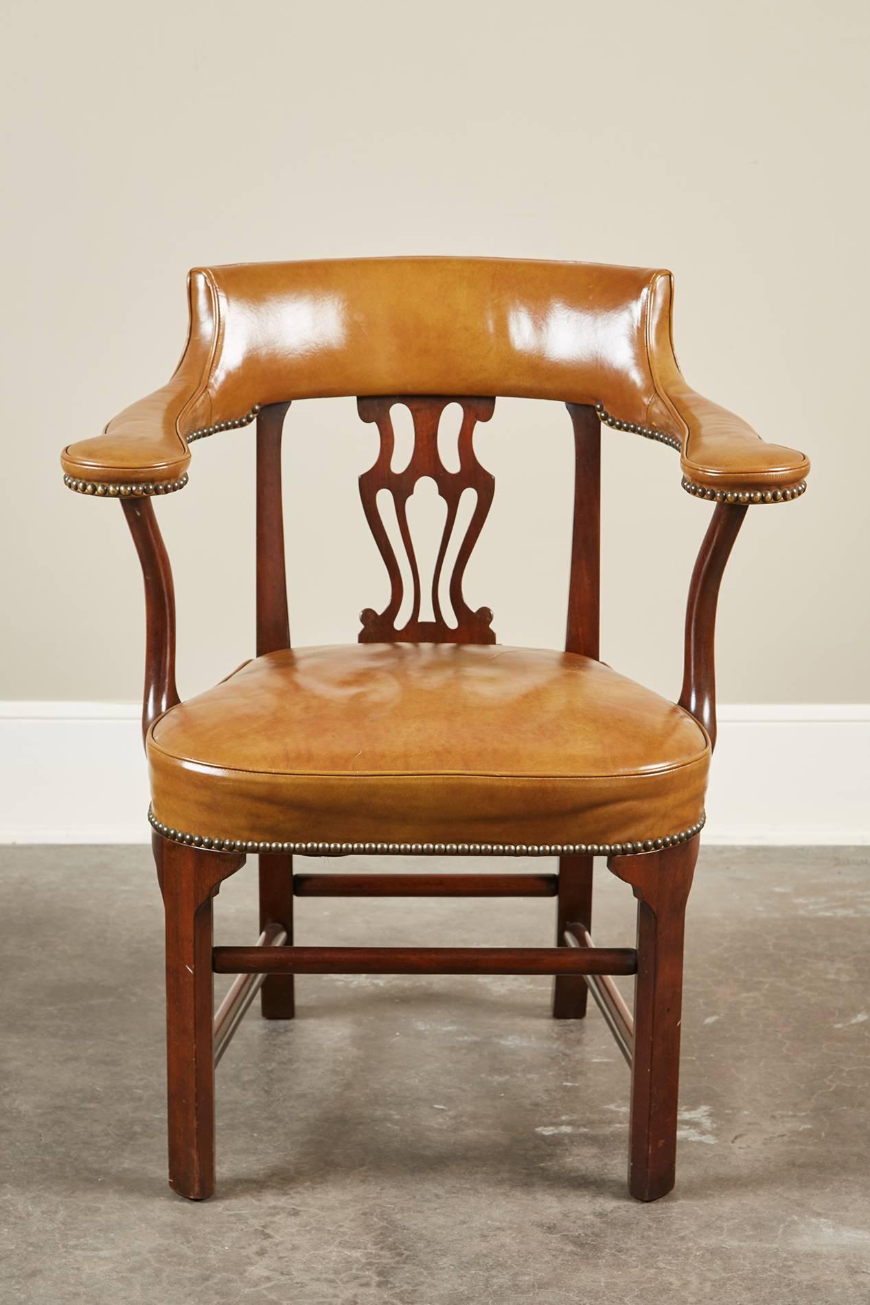 A unique pair of Mid-Century Modern American mahogany and leather armchairs with an abstract urn-like shaped splat. The crest rail is upholstered with the leather that continues onto the armrests and is held together by nailheads.  