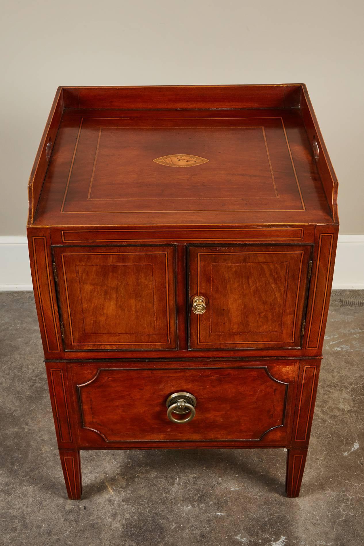 An 18th century English Georgian mahogany bedside commode table featuring inlay on the top of a center shell emblem, and consists of one drawer and two doors.