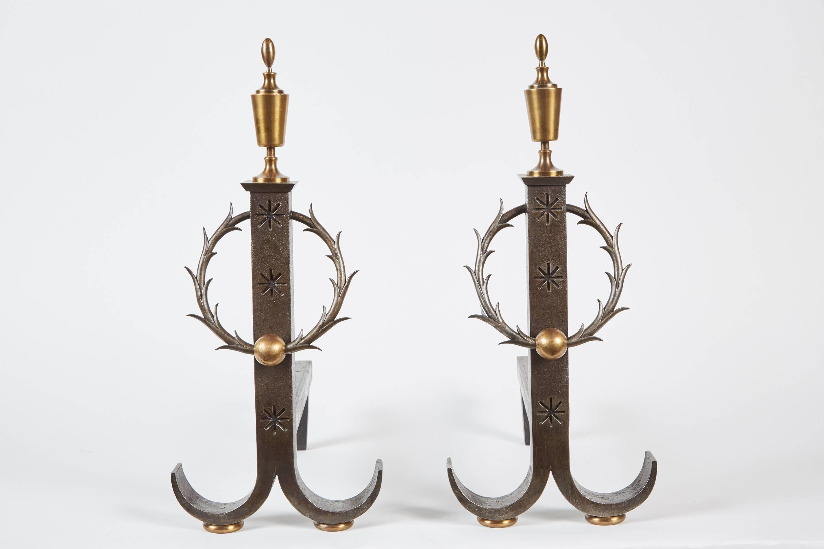 A handsome pair of late 19th-early 20th century wrought iron andirons by Samuel Yellin. The two feature finials on each andiron, a body with carved star designs and a centre wreath.