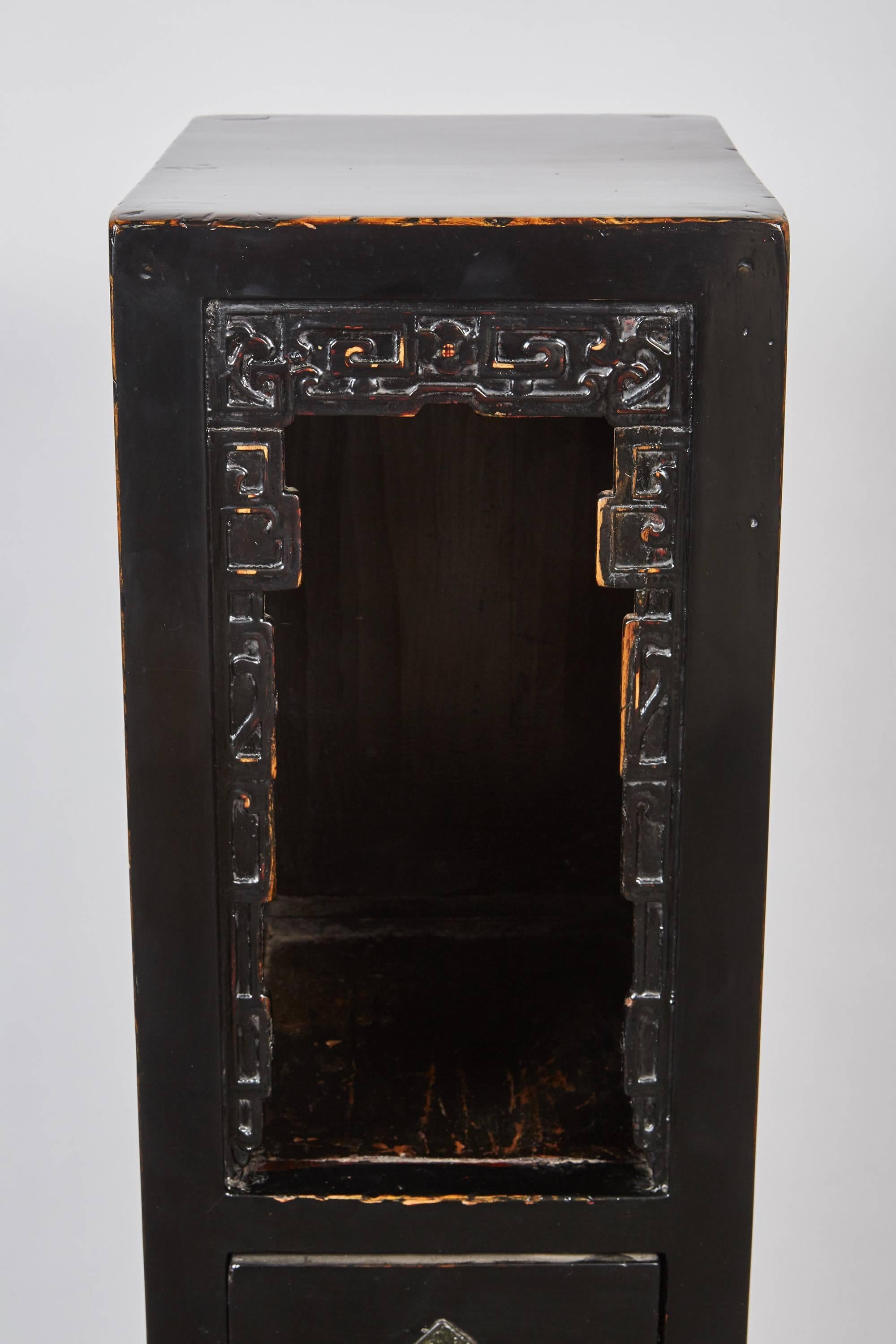 A one of a kind late 18th century Chinese, Qing dynasty black lacquer one door, one drawer tall tea table that has beautifully carved designs in the shelving area just above the drawer and door with brass hardware.