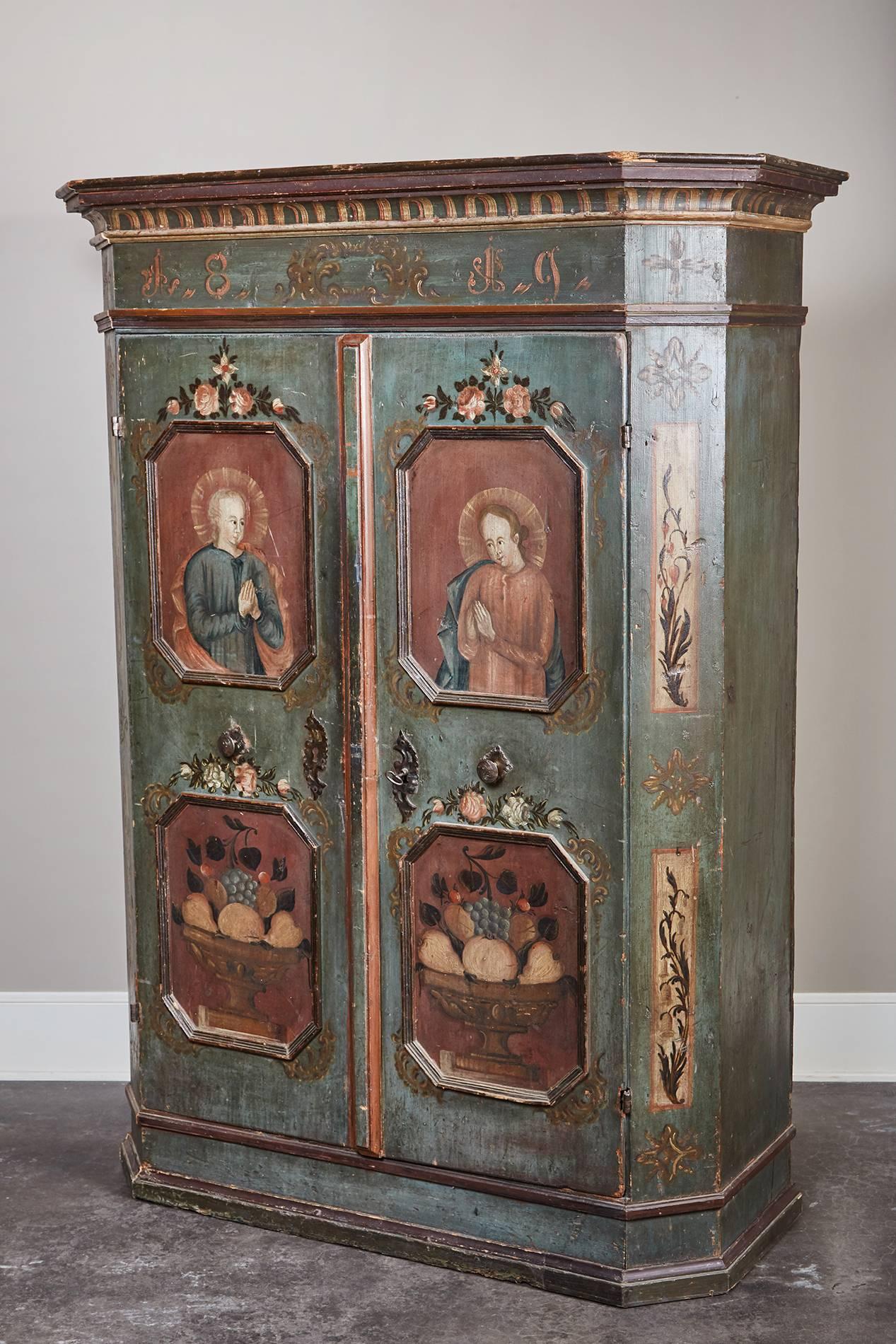 An early 19th century Southern German two-door cabinet with original paint and features design motifs such as stylized acanthus leaves, religious figures, and still life scenes. Dated in paint 1819.