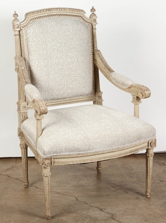 A pair of French late 18th Century carved Louis XVI arm chairs, newly upholstered in a subtle grey and white fabric with a swirling circular pattern. 
The arms on these Louis XVI chairs are padded, and the wood is carved in studded, linear and