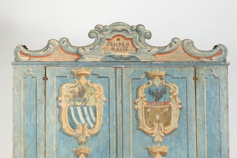 An 18th century painted Italian cabinet with two doors opening in the center. They are painted in various outlined plaques that represent coats of arms. They are blue paisley wall paper lined. The inside has three levels of shelving, also wallpaper