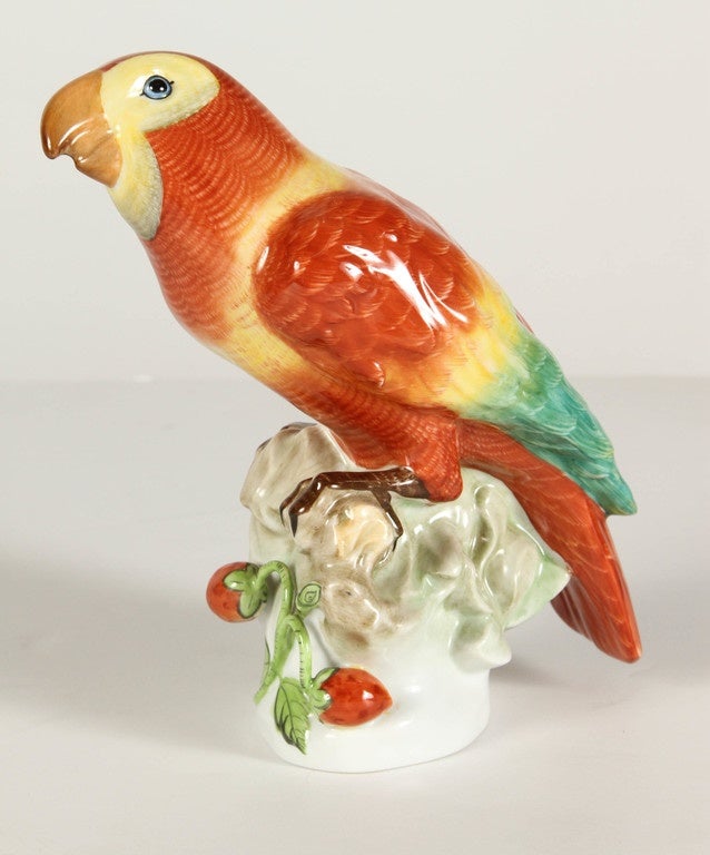 A 20th Century porcelain figurine of a sitting Parrot by Herend of Hungary. The brightly colored heron is depicted sitting on a branch, with its head cocked to the side. Its body is in an orange-brown color lightened in warm yellow, and his wings