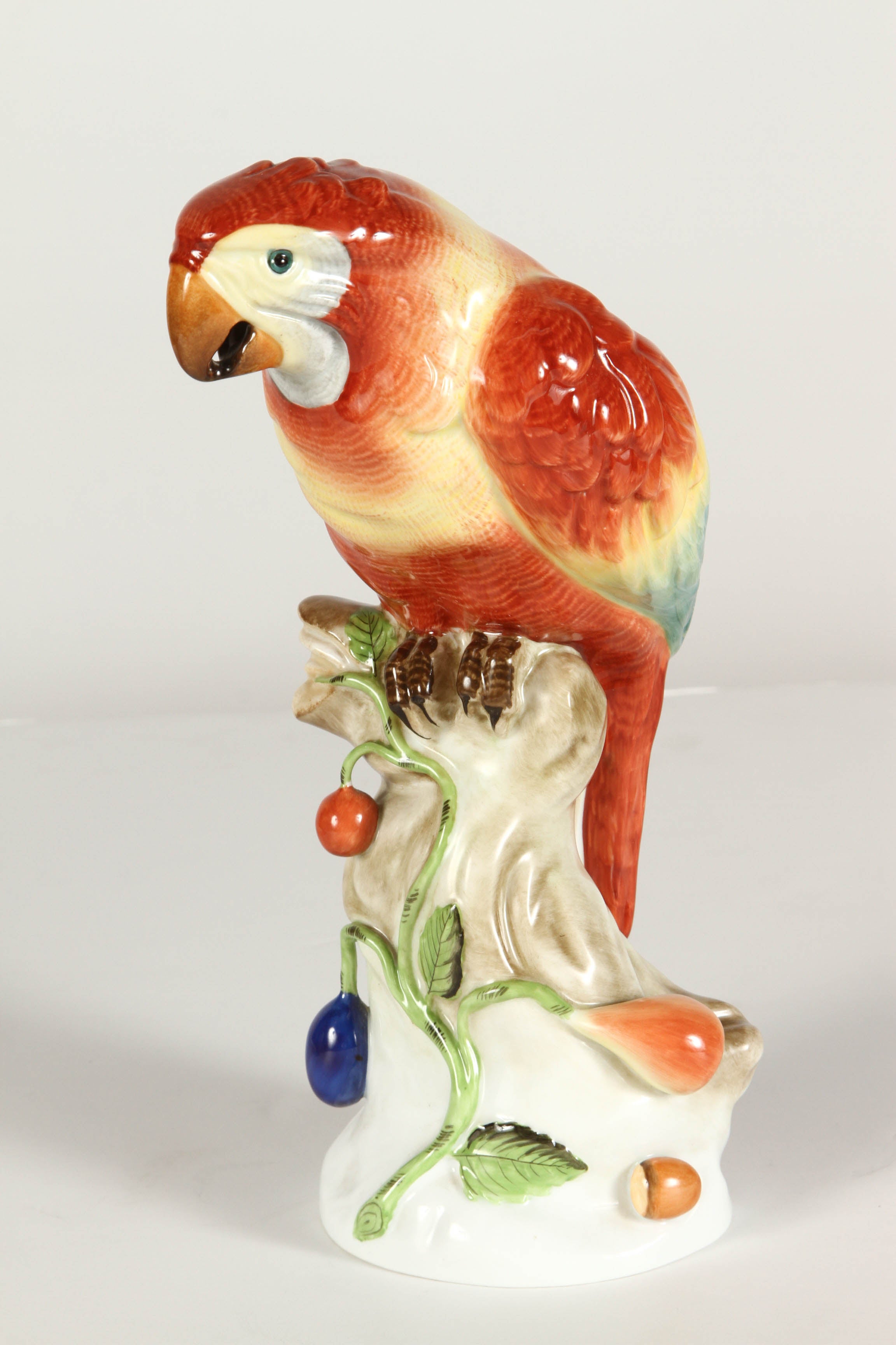 20th Century porcelain figurine of a sitting Parrot, created by Herend of Hungary. A bright-eyed heron with brown, yellow and blue green plumage is depicted sitting on a branch laden with fruit.
