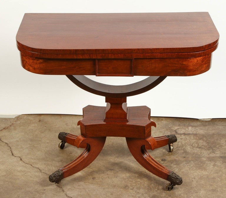 A 19th Century mahogany card table. The table top does open and it has a very fine gold decorative marking along the perimeter.  There are four feet at its base which curve in a scroll-like shape to end in cast brass casters.  There is some slight