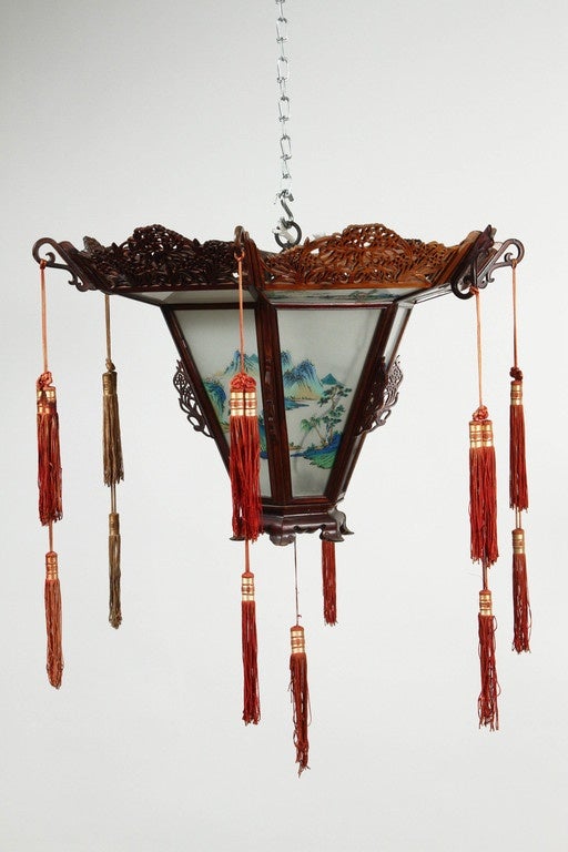 A 1940s rosewood and painted glass Chinese lantern. Each corner has a tassel in red and a gold colored accent. The glass panels are opaque and in two parts, and each has painted scenes of trees in blue. The rosewood frame is elaborately and finely