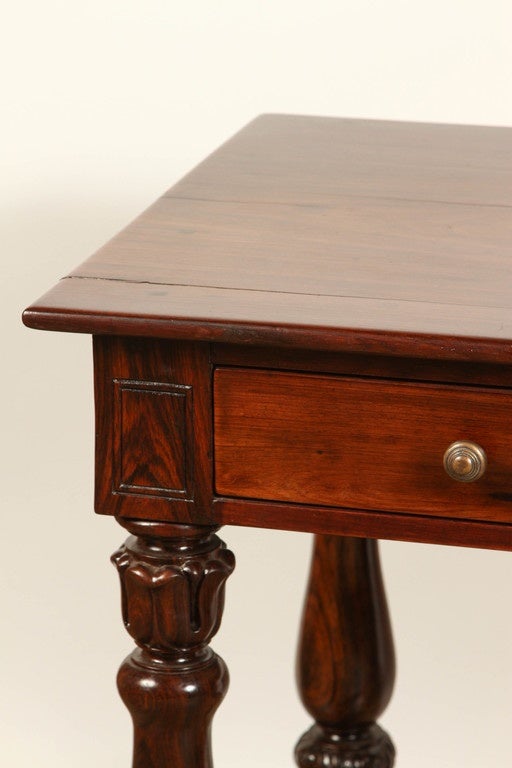 An elegant early 20th Century French Colonial desk in rosewood.  There are three small drawers at the front.  The knobs are new. This early 20th Century rosewood desk has Victorian design elements, a lovely finish and beautifully turned legs.