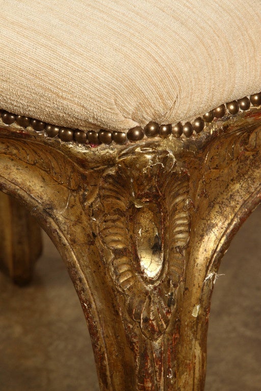 Gilded Louis XVI carved stool, French, circa 1850. The stool is upholstered in a cream colored fabric, and the frame of this Louis XVI stool is topped with a row of a studded pattern just below the upholstery. The base and its gently curved legs are