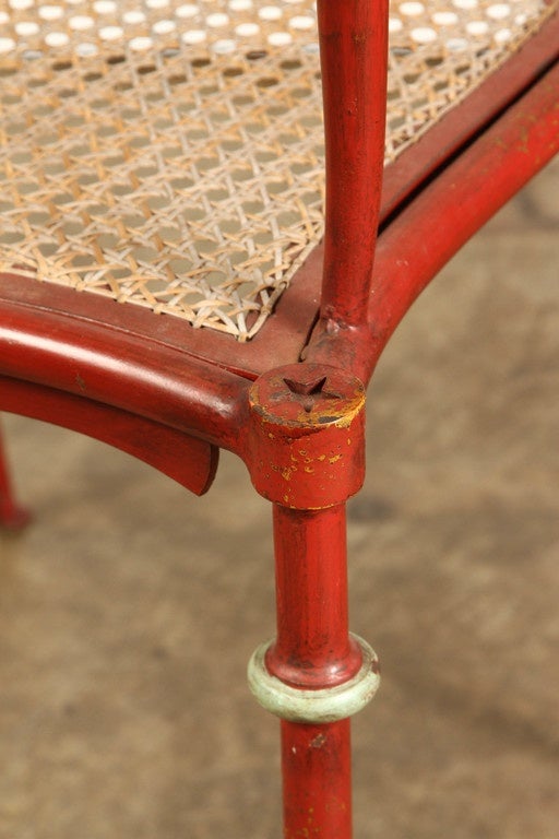 An intrically detailed Austrian red iron armchair, circa 1910. This red iron chair has a cane seat and its legs and arms are delicately curved. The seat back has circle and star shapes cut out in a stencil fashion across the top, as well as five