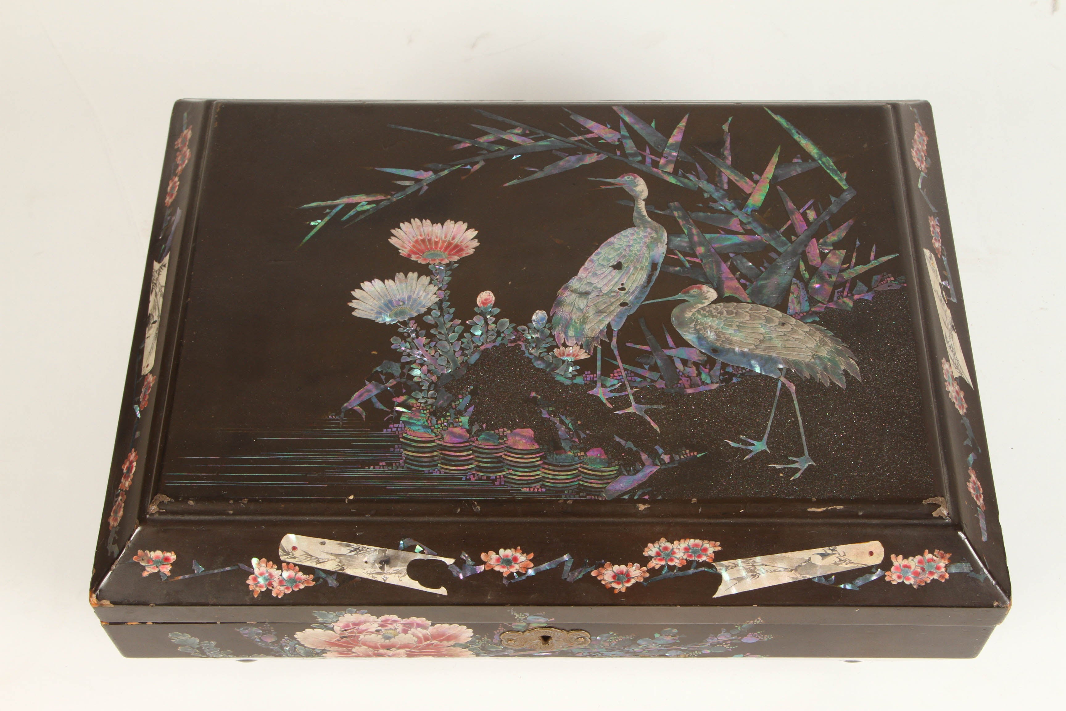 A lacquered and mother of pearl inlaid Japanese sewing box. This Japanese lacquered box is decorated in scenes of cranes and flowers. Inside, the box has numerous small separate areas for sewing supplies.