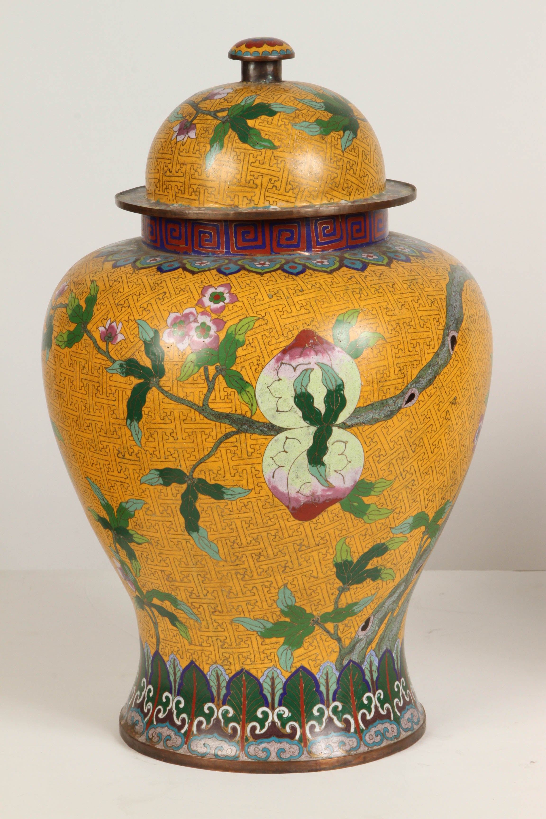 A stunningly beautiful 20th c. Chinese cloisonne temple jar with a yellow background and a peach tree branch depicted across the body of the jar. 