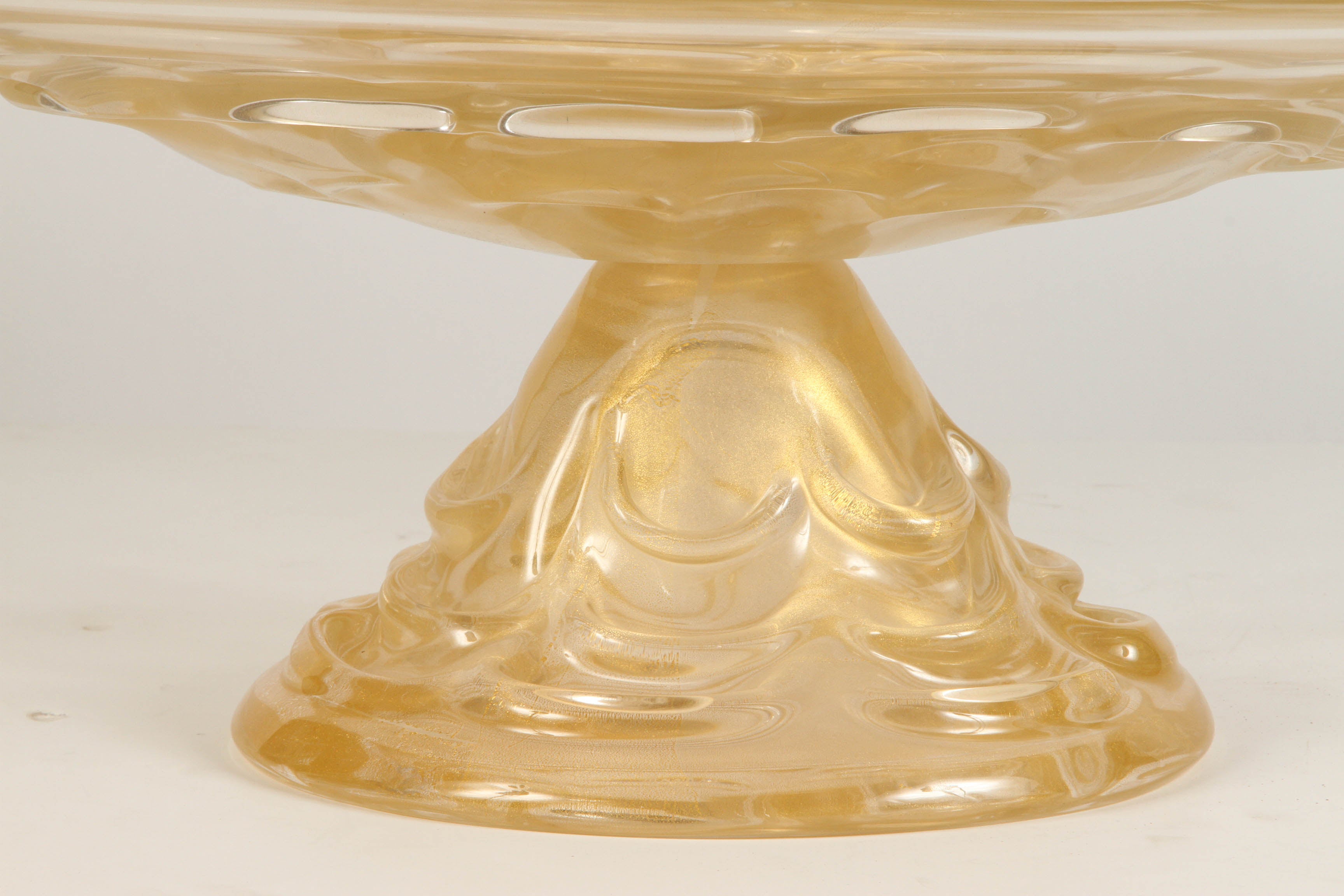 A 20th Century oval Murano pedestal bowl in glass that is light golden in color, and designed in a swag sort of pattern about the base. The foot is tall, at 9 inches. This Murano glass bowl is circa 1980.