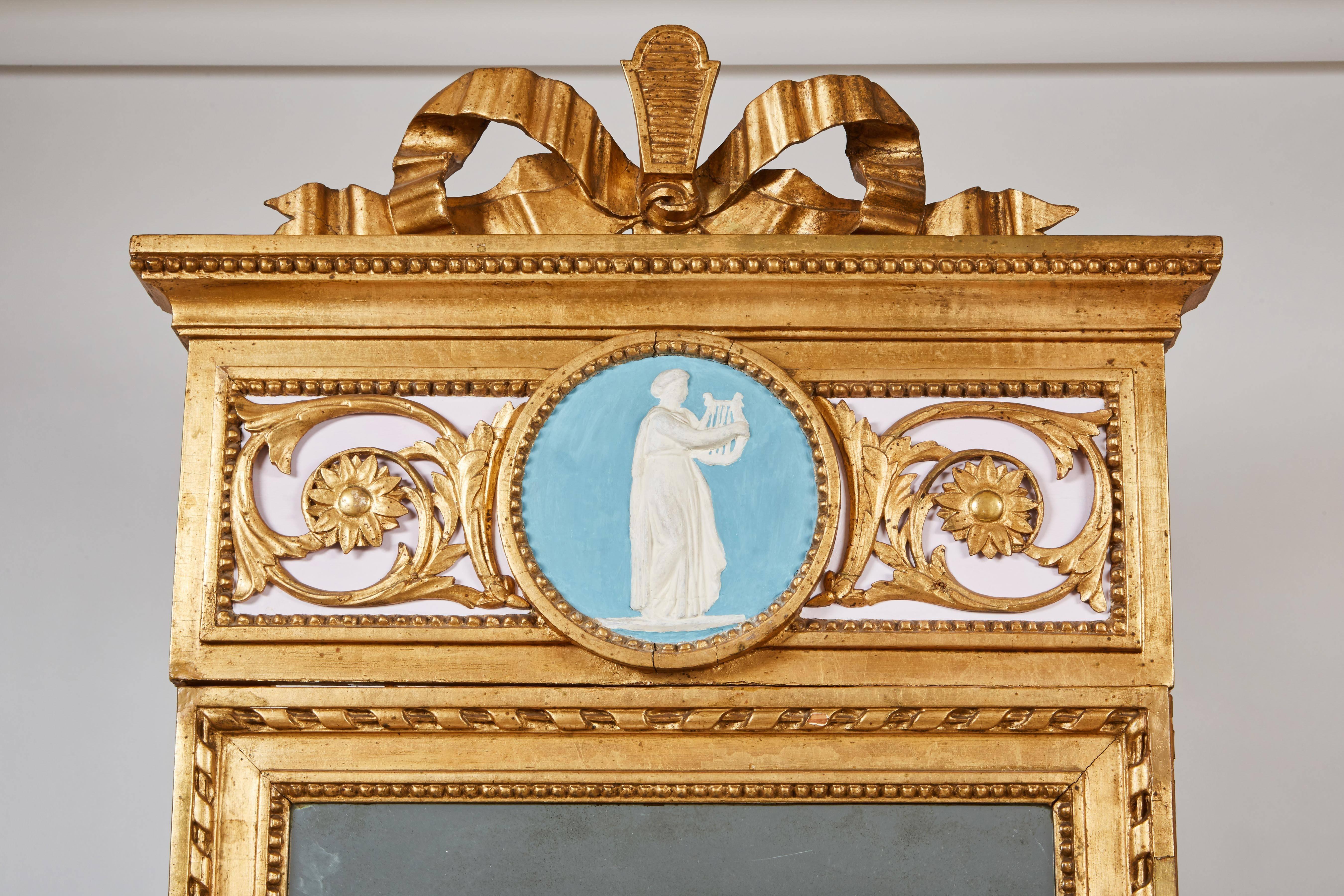 La console avec un plateau en marbre blanc veiné, la frise sculptée de motifs feuillagés et le médaillon central sur des pieds fuselés et cannelés. La plaque de miroir rectangulaire dans une bordure robée surmontée d'une crête supérieure