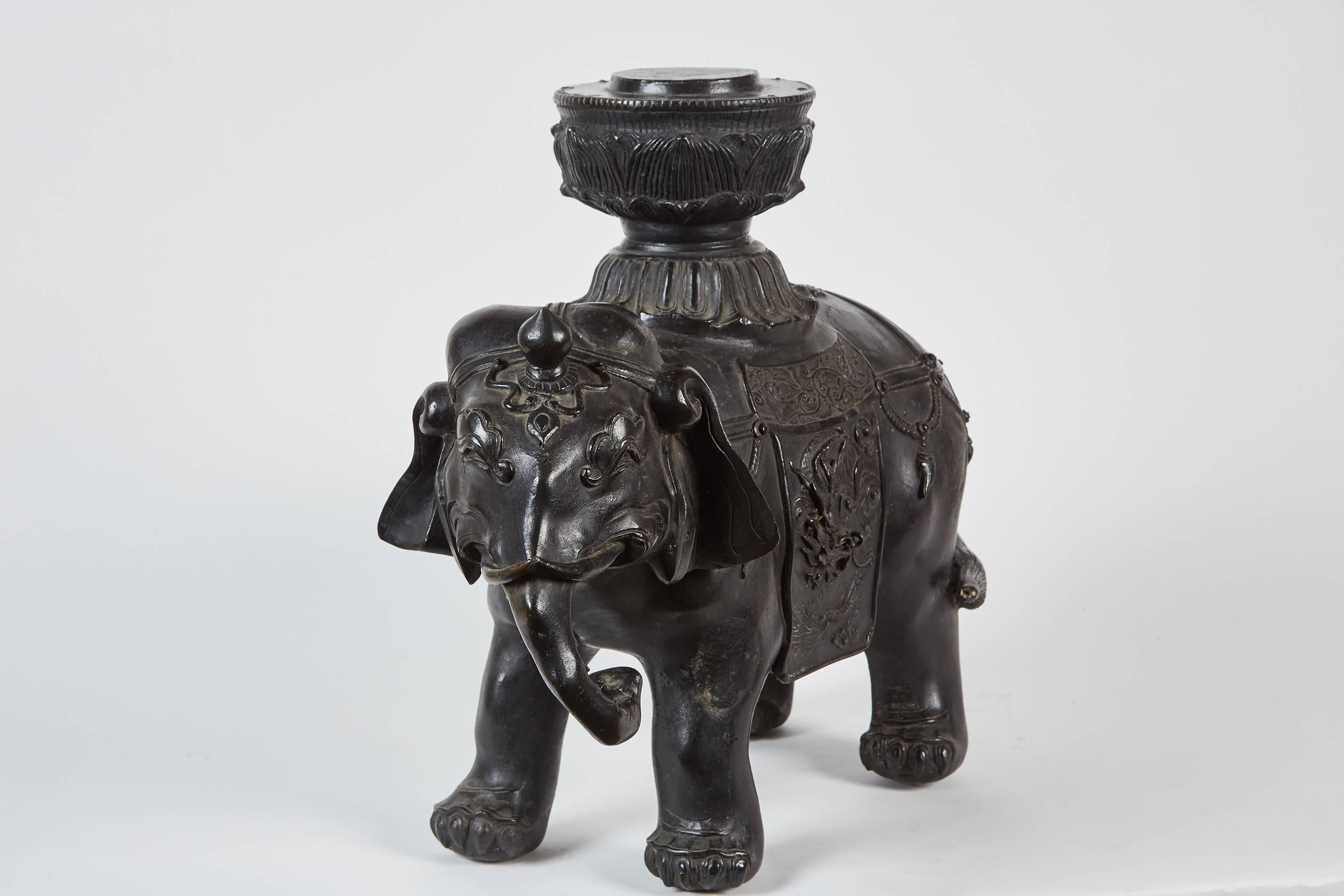 A medium sized 19th century Japanese bronze elephant that could possibly be from a temple in Kyoto, Japan. The piece features an elephant with a howdah, or a decorative cloth over the elephants body. The howdah has design elements such as a dragon,