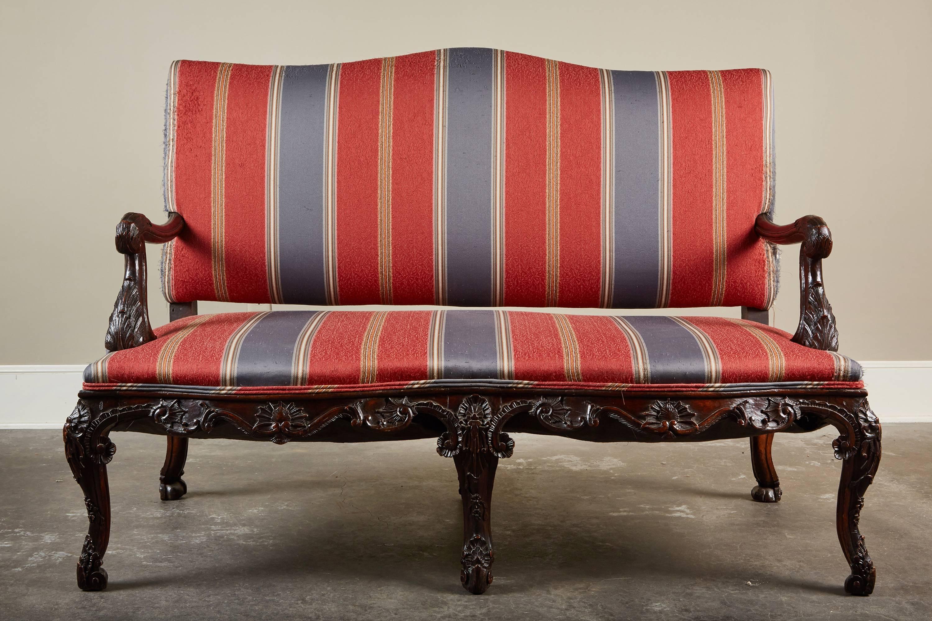 A 17th century Italian carved settee that features typical design elements of the Rococo period, such as intricate carvings of foliage motifs throughout the wood frame and cabriole legs. 