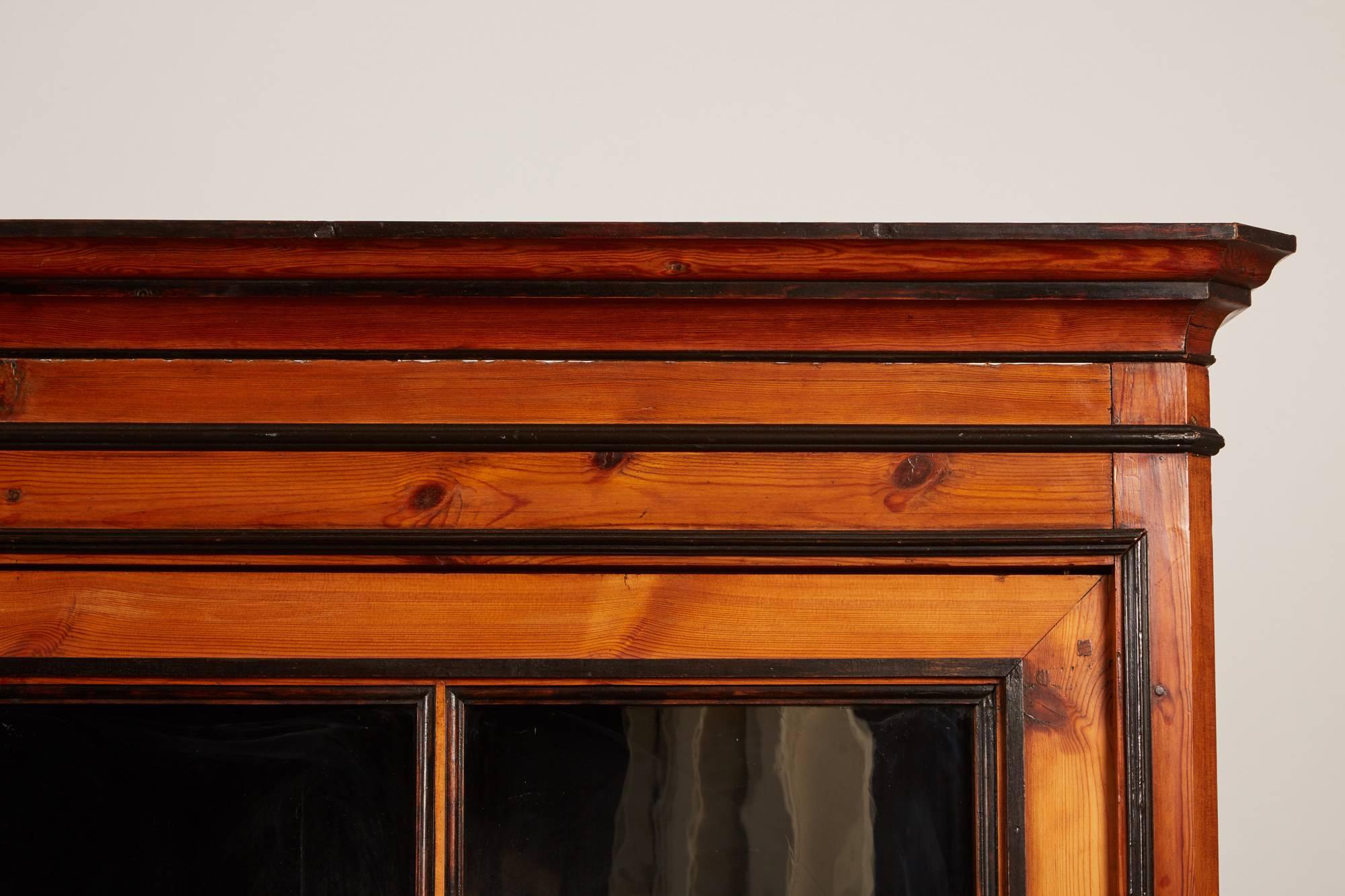 19th century English pine cabinet with pair of large glass doors. Black painted interior and dark trim through front of front face. Simple cove moulding on top edge and feet. The shelves are adjustable