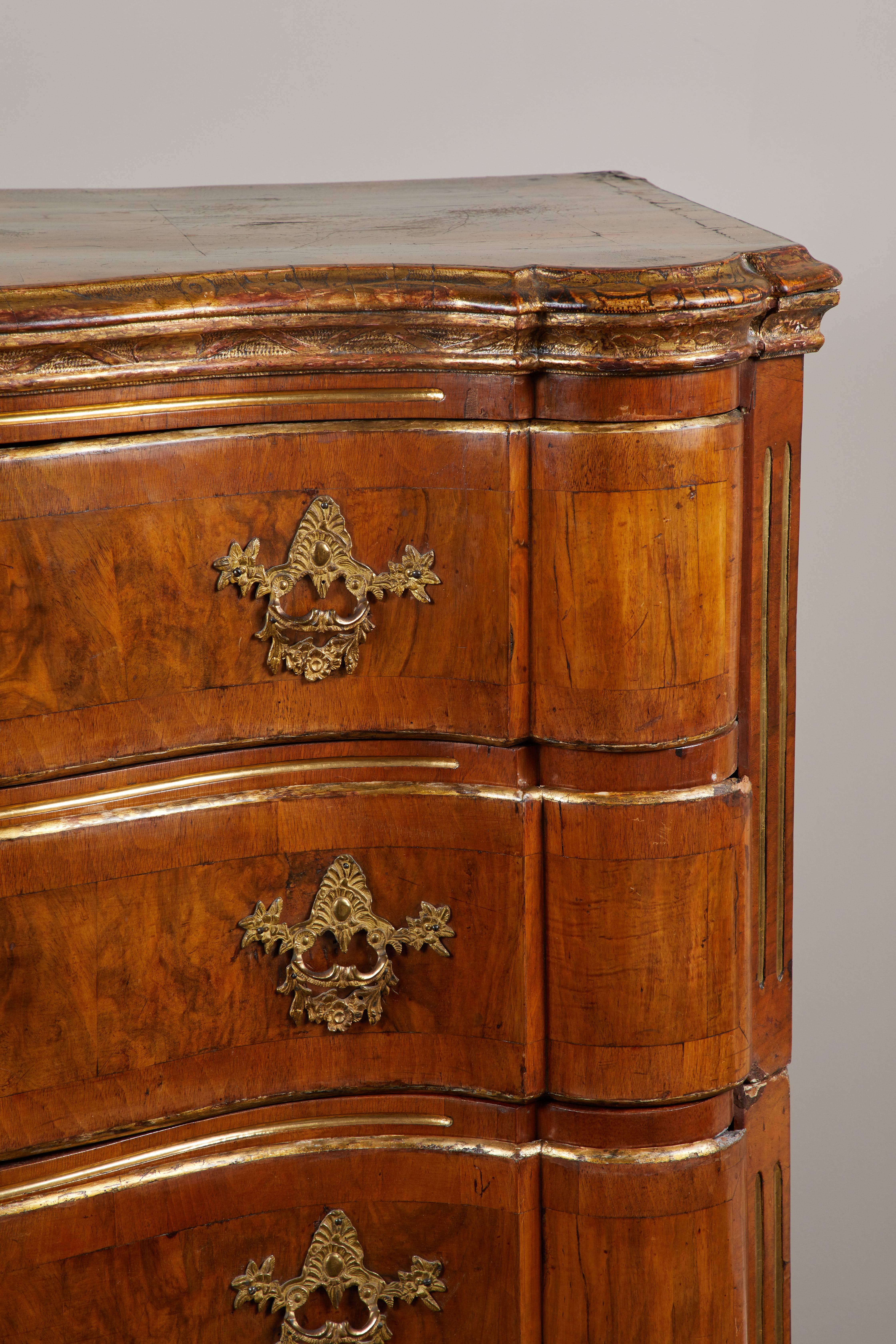 An extraordinary 18th century Danish Rococo walnut chest of drawers. Serpentine shaped front and sides featuring original handles and hardware, with crossbanded drawer fronts. Gilt edge detailing, and stands on carved, gilt legs. Splits in three