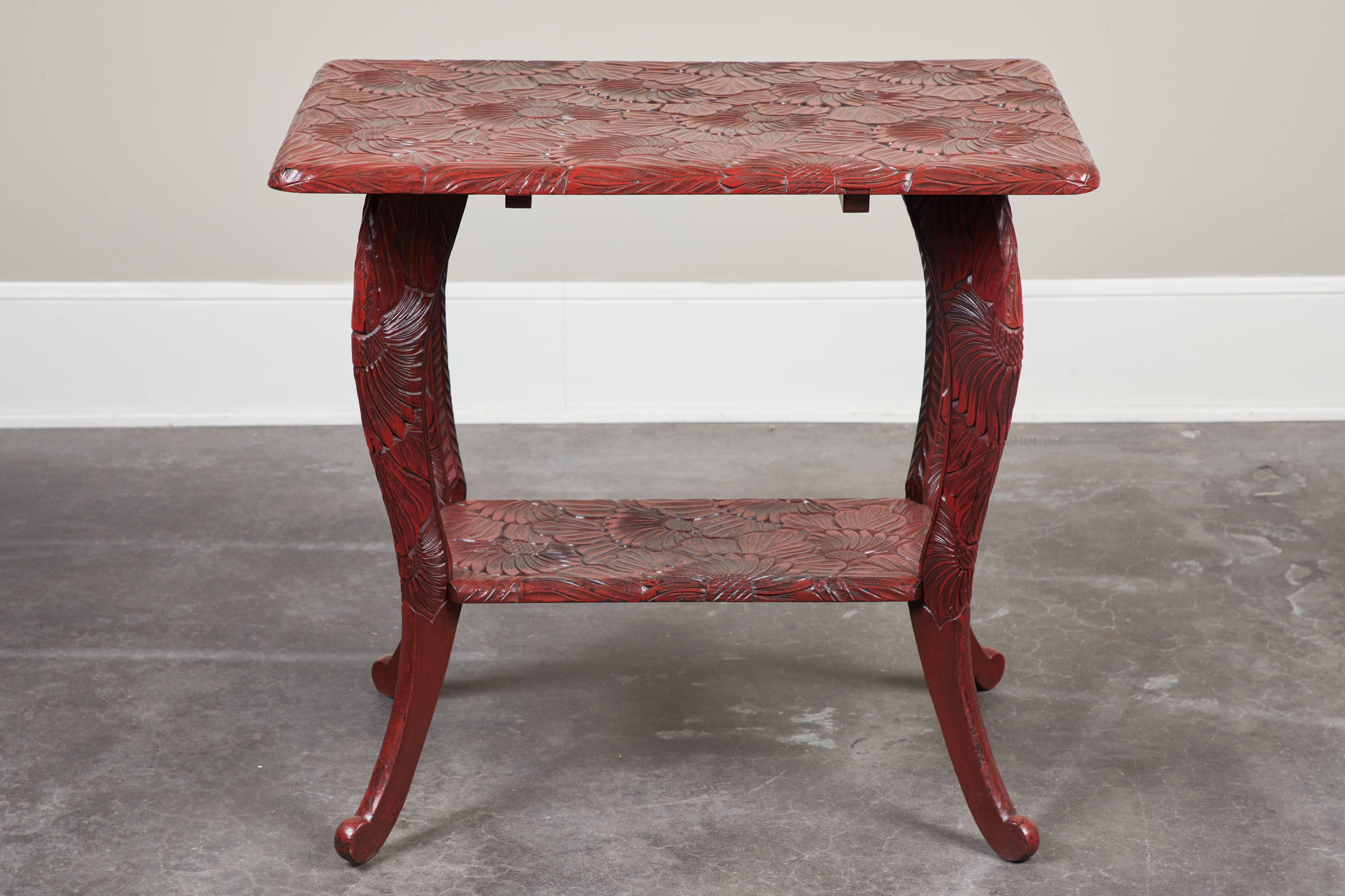 An early 20th century intricately carved floral red lacquer side table with a single shelf inside splayed legs.