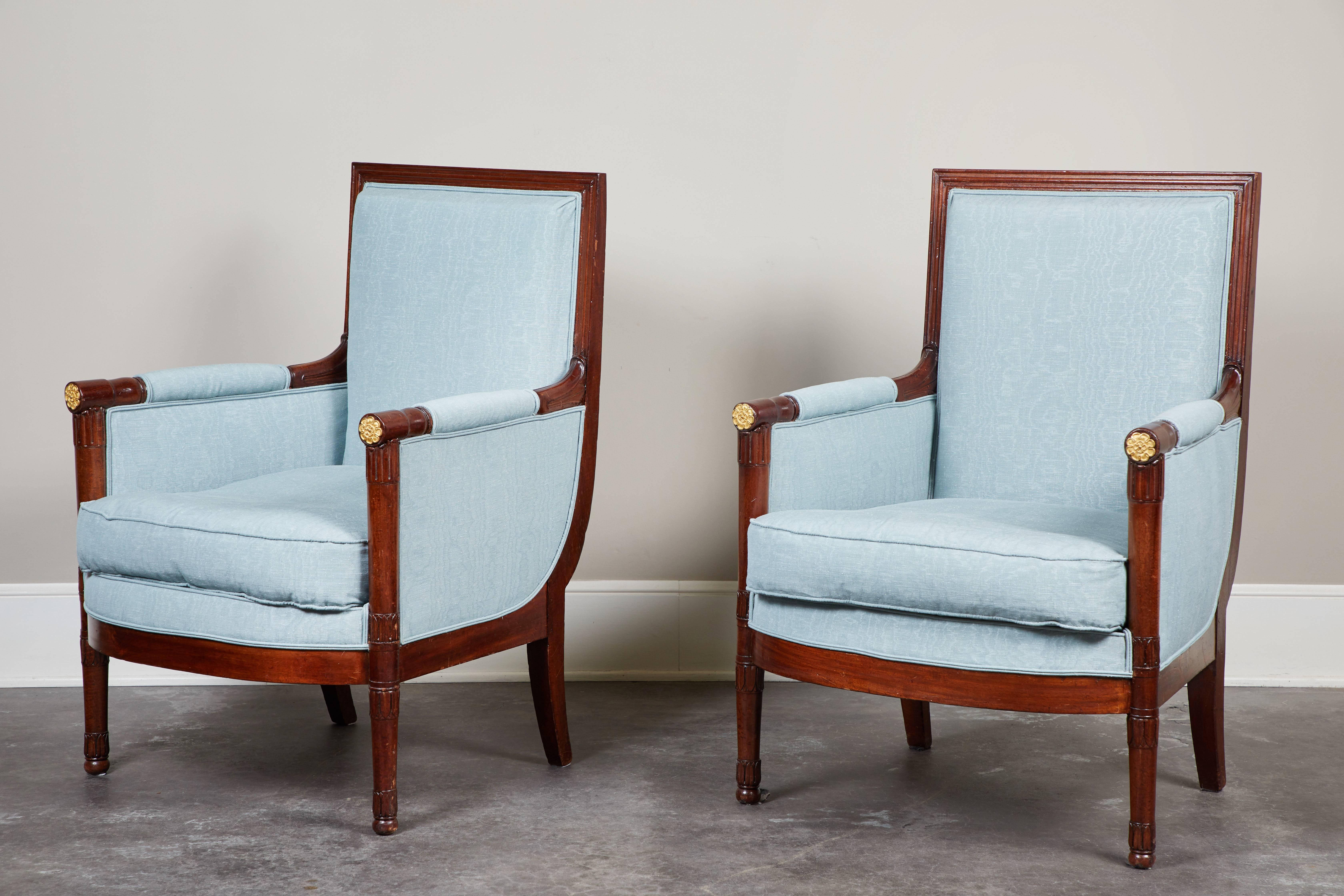 A handsome pair of French Empire mahogany bergeres, circa 1810. Turned legs with foliage carving details and brass trim details.