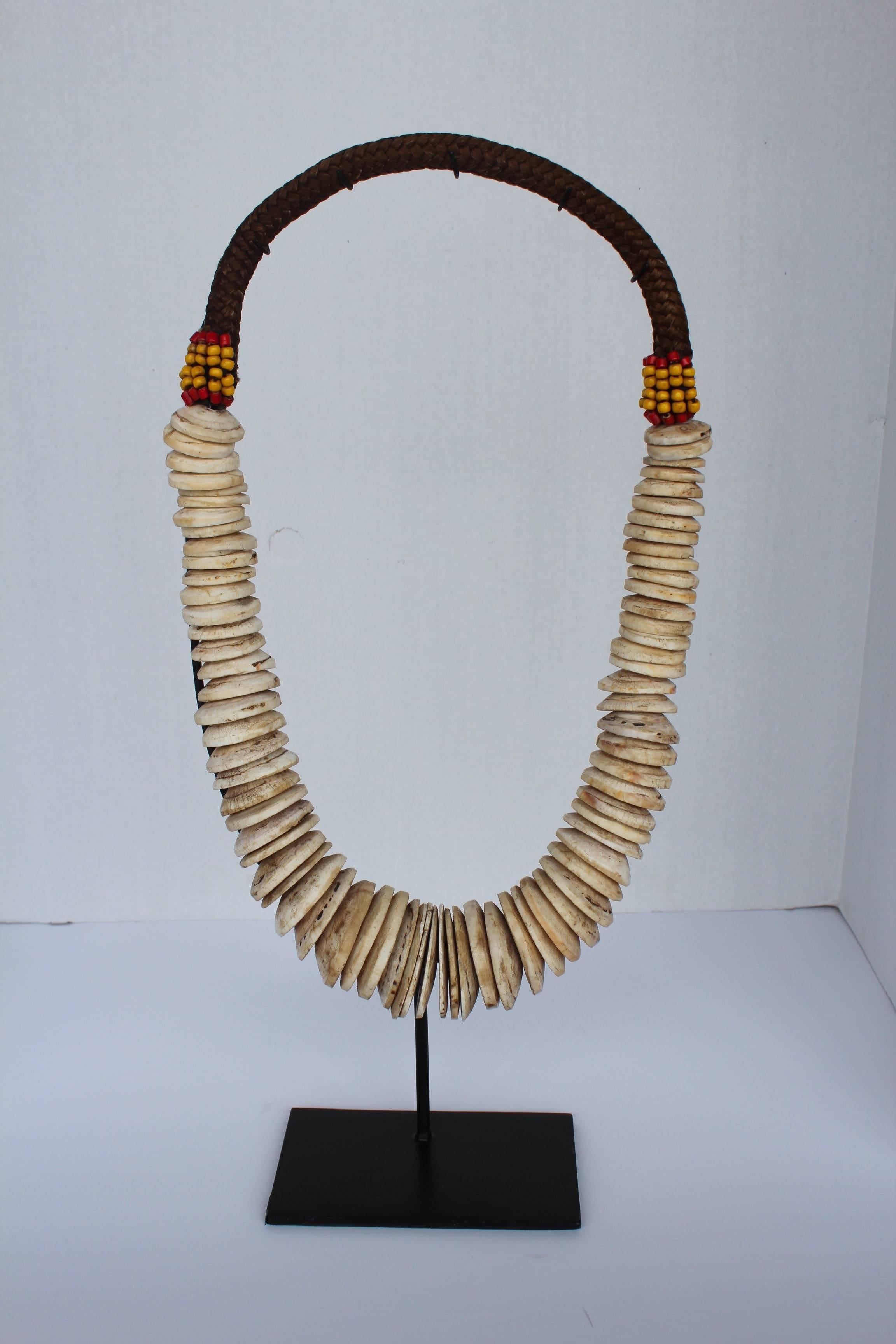Handmade vintage tribal necklace is decorated with small yellow and red beads surrounded by cowries on handwoven hemp with full grown 90 conus shell discs on a black custom stand. 

The shell disc have been chiseled and polished from a traditional