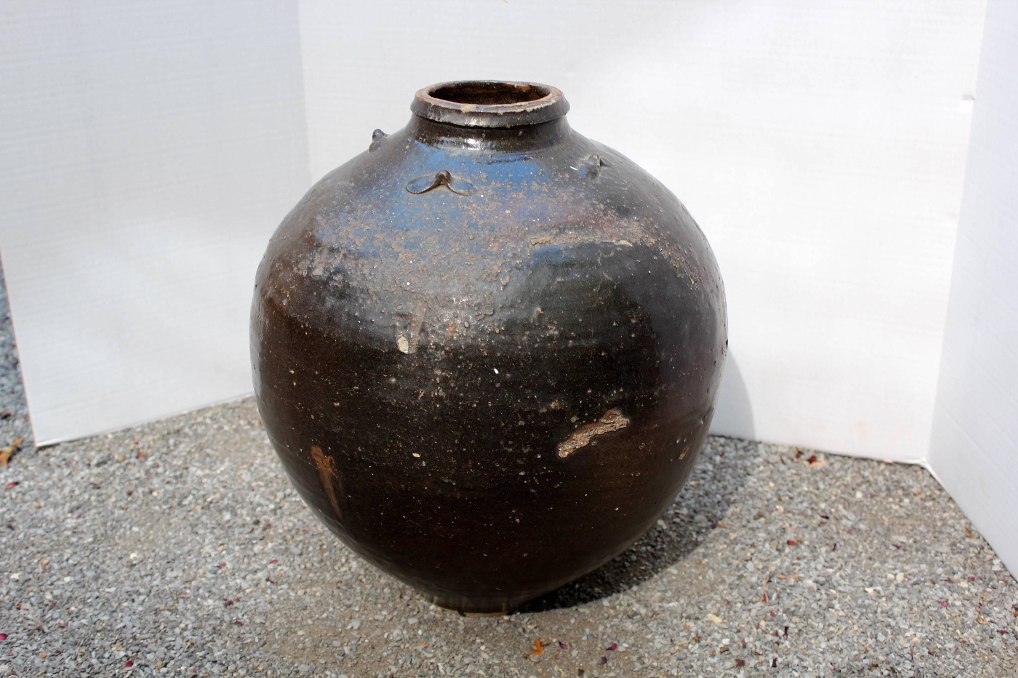 Antique Asian storage jar.
Stoneware with dark brown iron glaze jar with four texture lugs around the top. 
Oviform jar with baluster shape top and bold glazed texture.