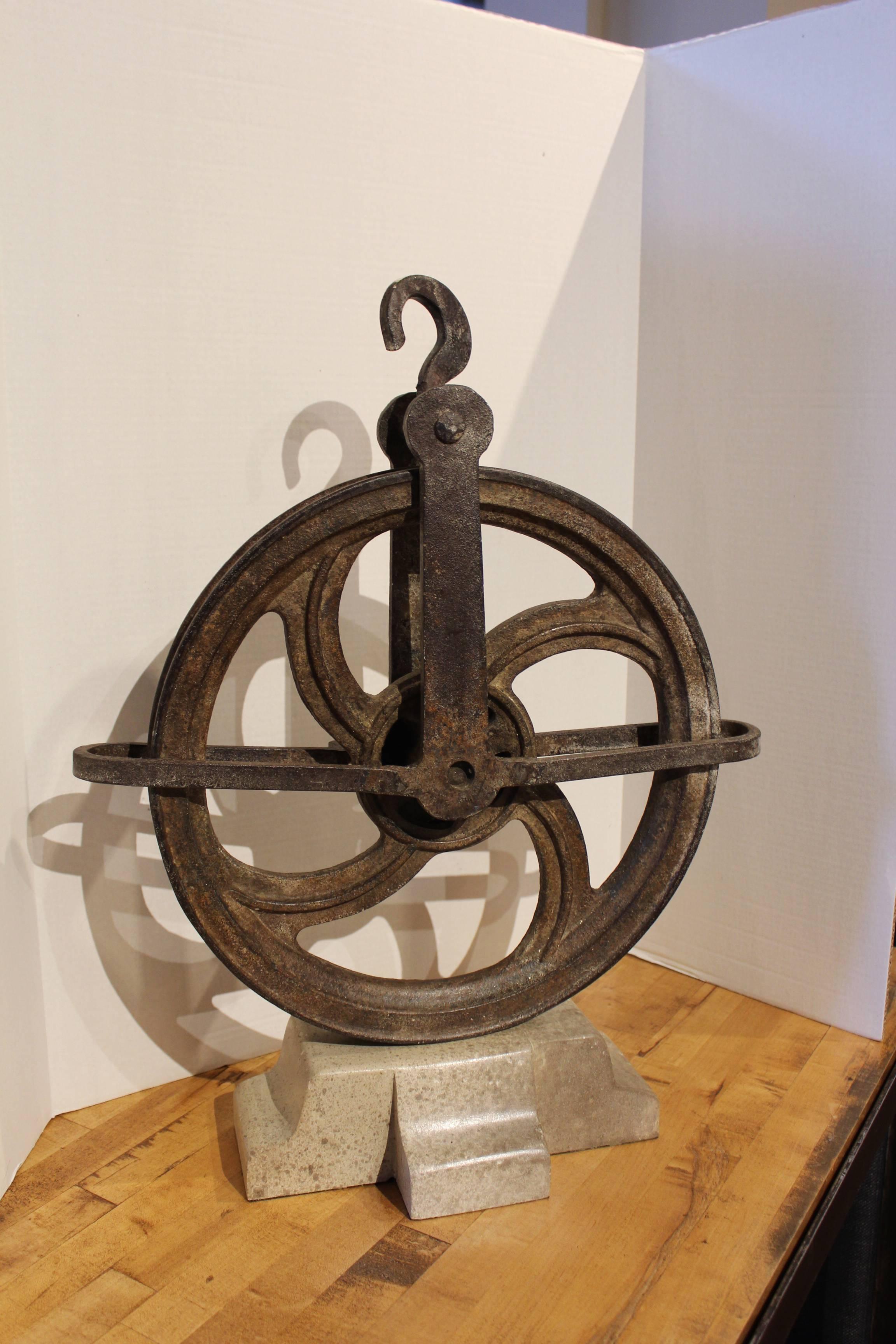 French tradesman pulley wheel decor. 
Primitive, cast iron pulley wheel. 
Distressed limestone mount base, 
circa 1900.