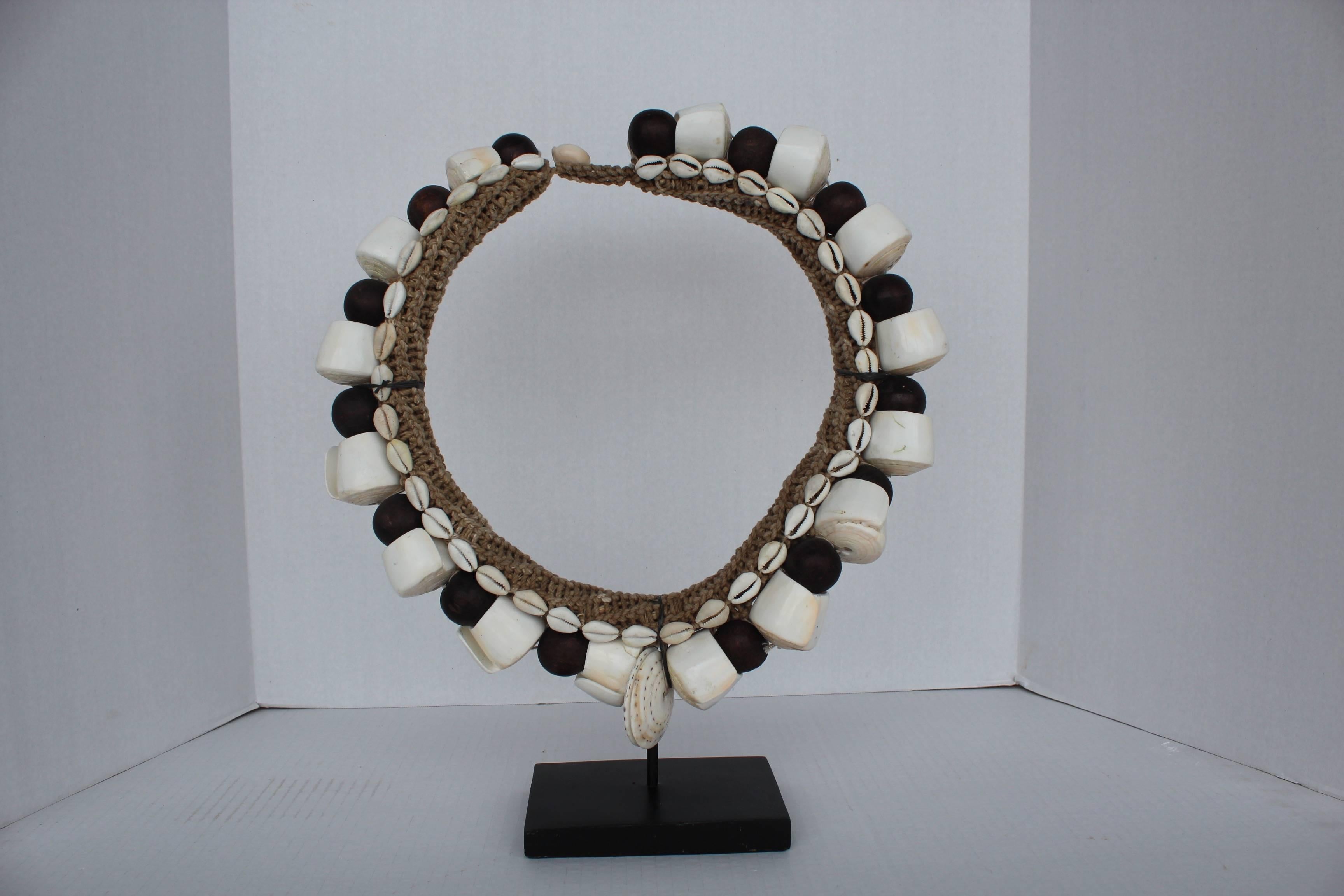 Polished and honed claim shell tribal pendant with handwoven fiber hemp, surrounded by cowrie shells, vintage pearl white curved shells, and coconut carved balls on custom Stand. 

A symbolism for wealth and pride, these necklaces were wrapped and