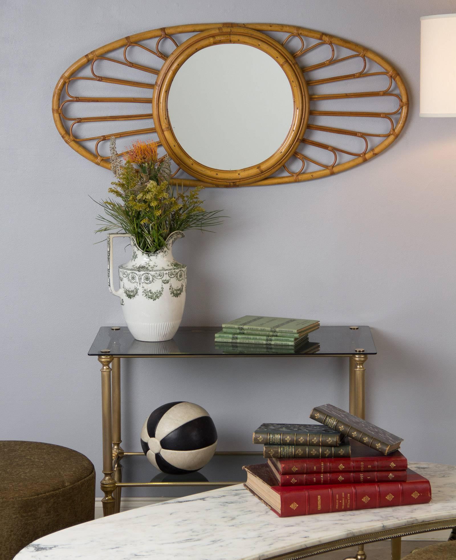 A very decorative round vintage mirror, circa 1960s, with an oval bamboo and rattan frame that can be hung either horizontally or vertically. The glass itself measures 15" in diameter.