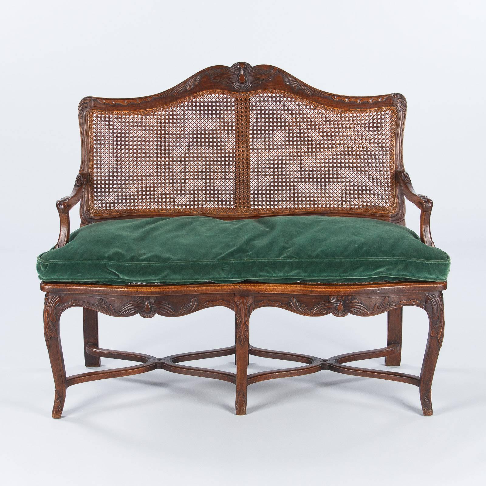 A very attractive caned bench with a walnut frame made in the Louis XV Style, circa 1900s. The bench features an arched back, curved armrests and a scalloped apron with acanthus leaf and shell carved designs. The bench rests on six legs that are