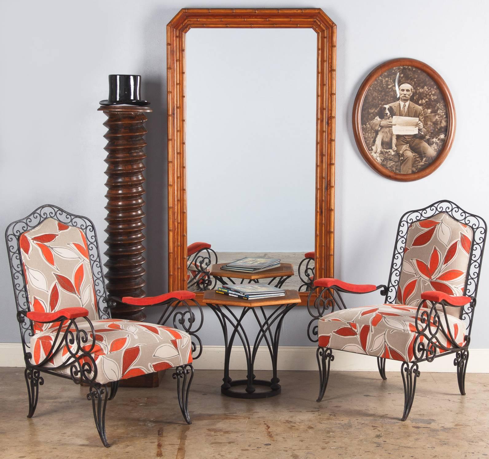 A great pair of French 1940s wrought iron armchairs that were recently re-upholstered with a colorful fabric featuring leaf motifs in light grey, red, orange and coral tones. The black iron frames are all scrolled. The seats are firm and