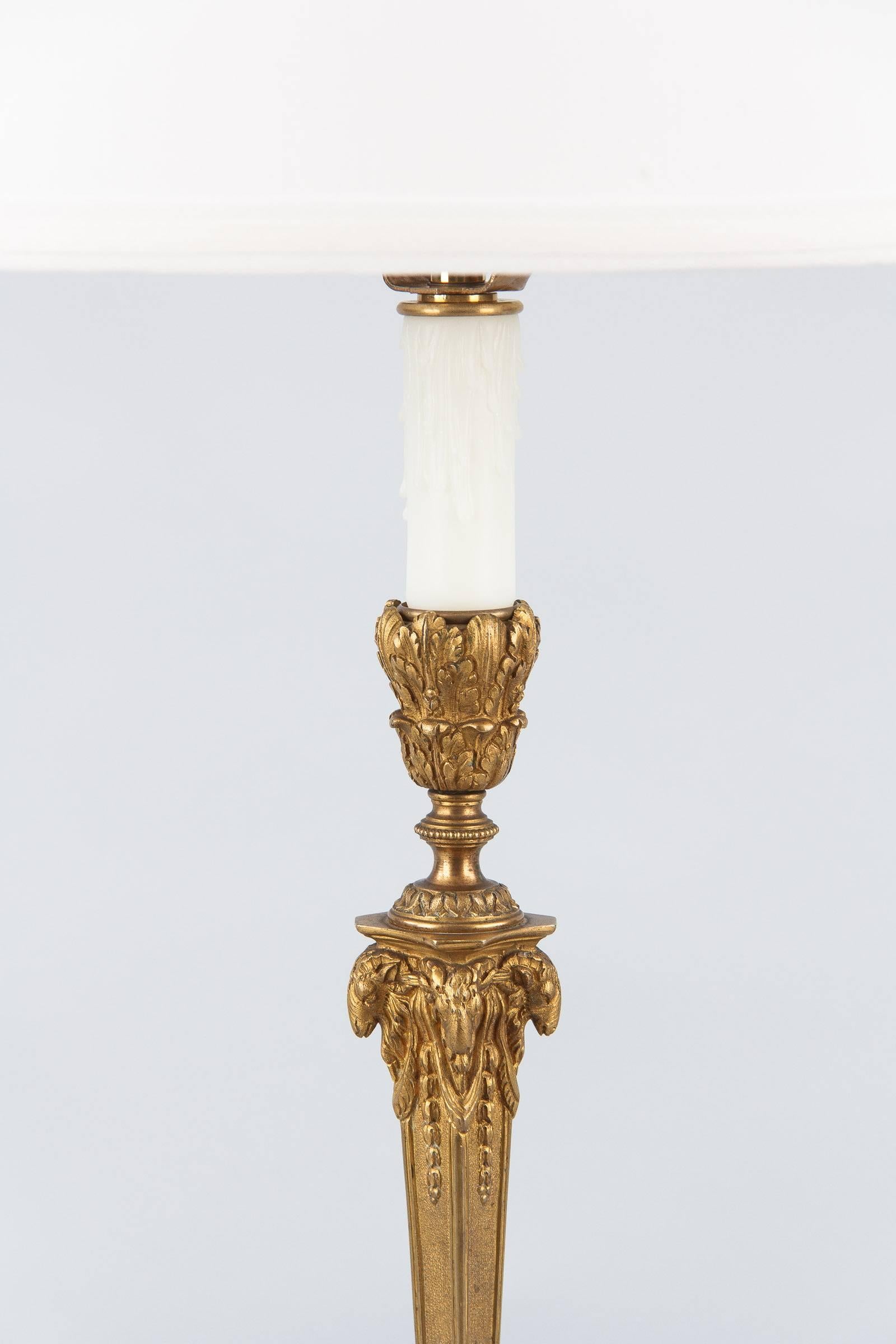 A Napoleon III period candlestick that was electrified, circa 1870s. The table lamp is made of gilded bronze with delicate chiseling and rams head design. The lamp has been rewired for a three-way bulb. The new drum shade is 10" height x